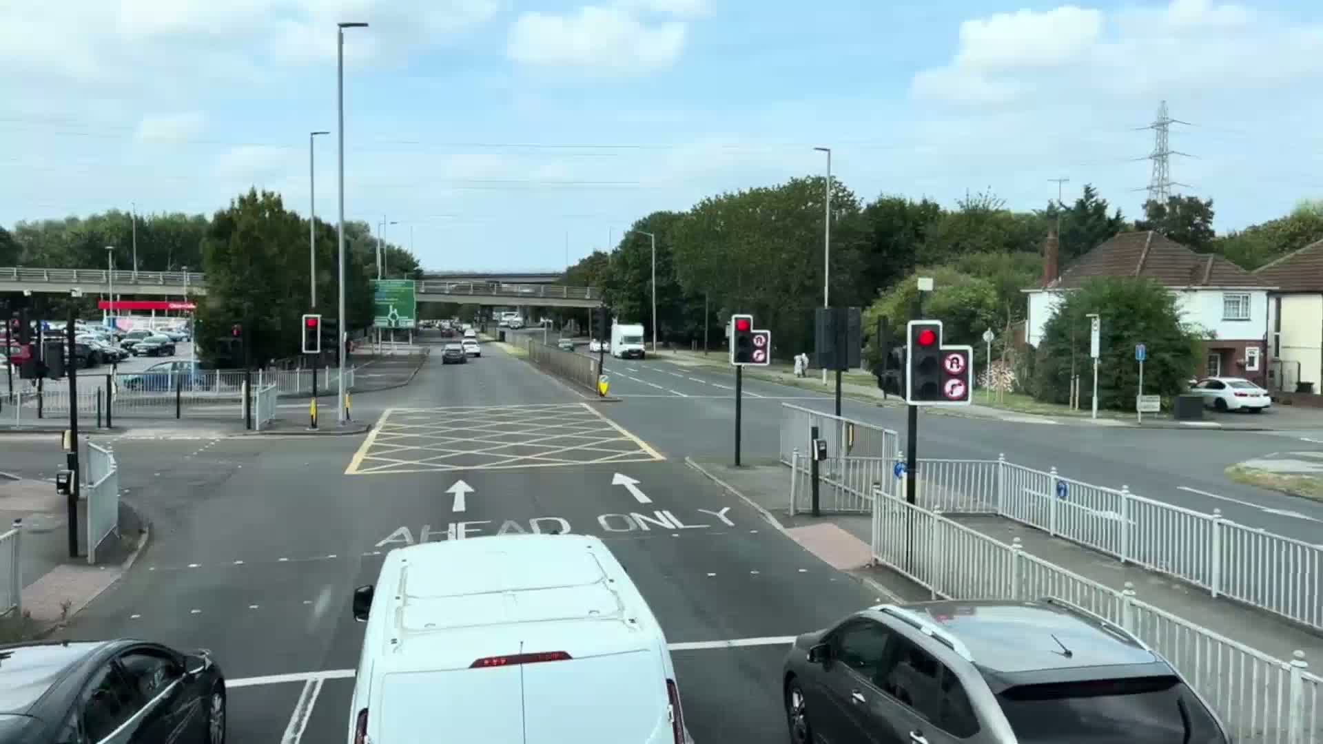 A road intersection with traffic lights, several cars, and a van, under a partly cloudy sky.