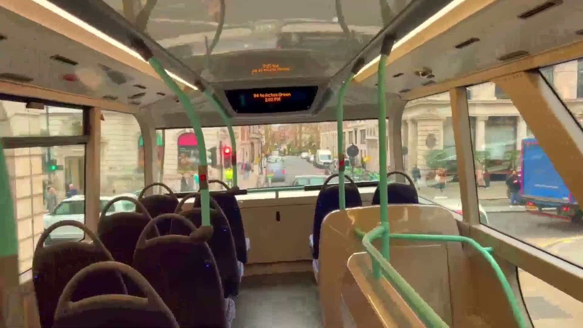 The mostly empty upper deck of a double-decker bus shows a view of a city street on an overcast day.