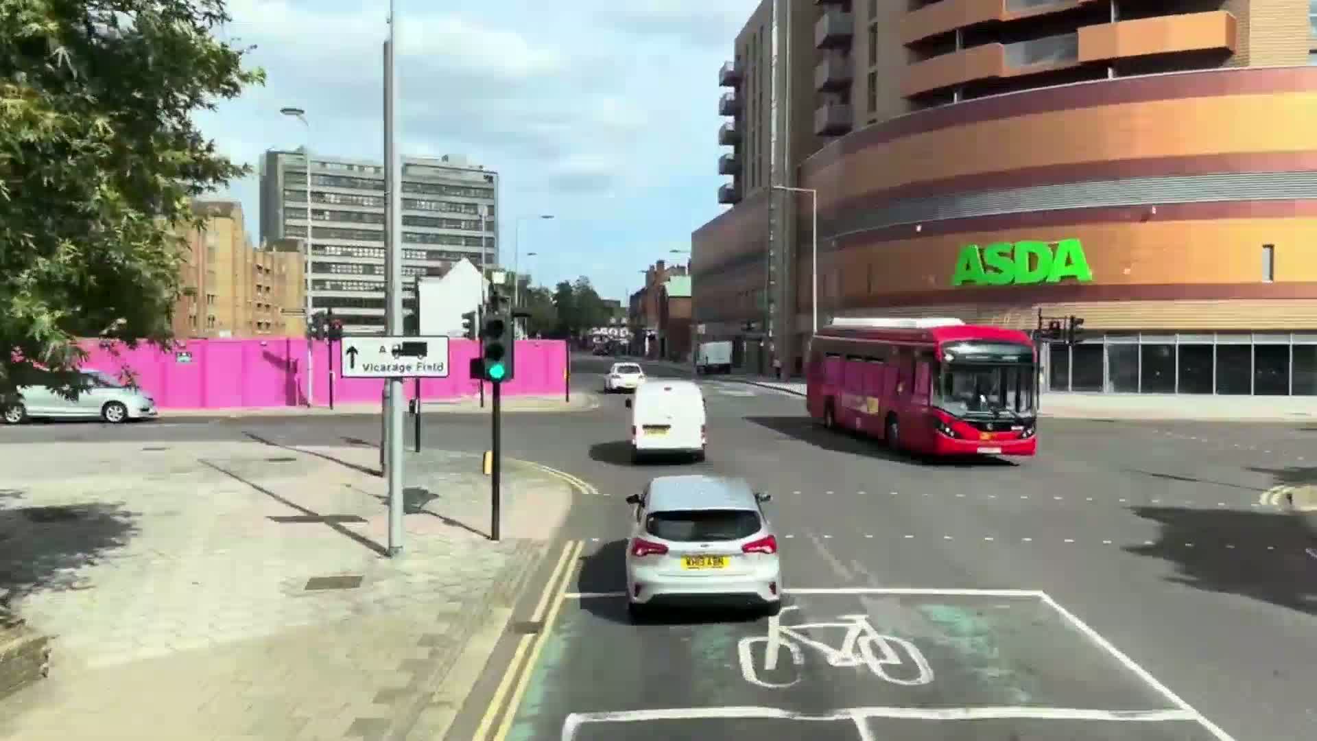 On a sunny day, several cars and a bus navigate a city intersection near a large building.