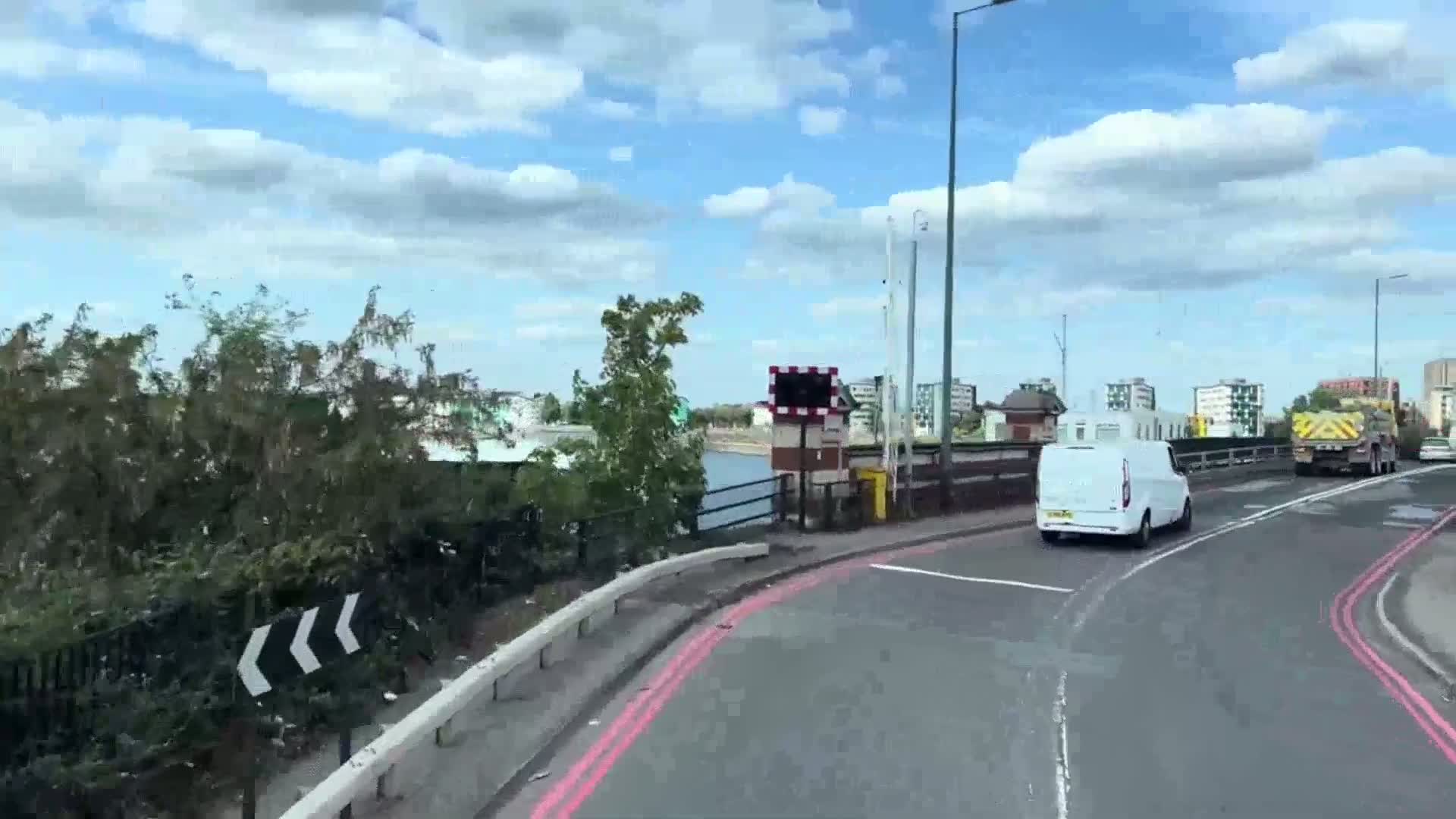 A white van drives on a bridge under a partly cloudy sky, with other vehicles and buildings visible in the distance.