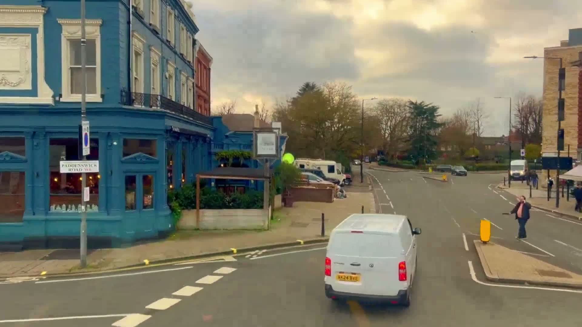 A white van approaches a crossroads near a teal-colored building on an overcast day.