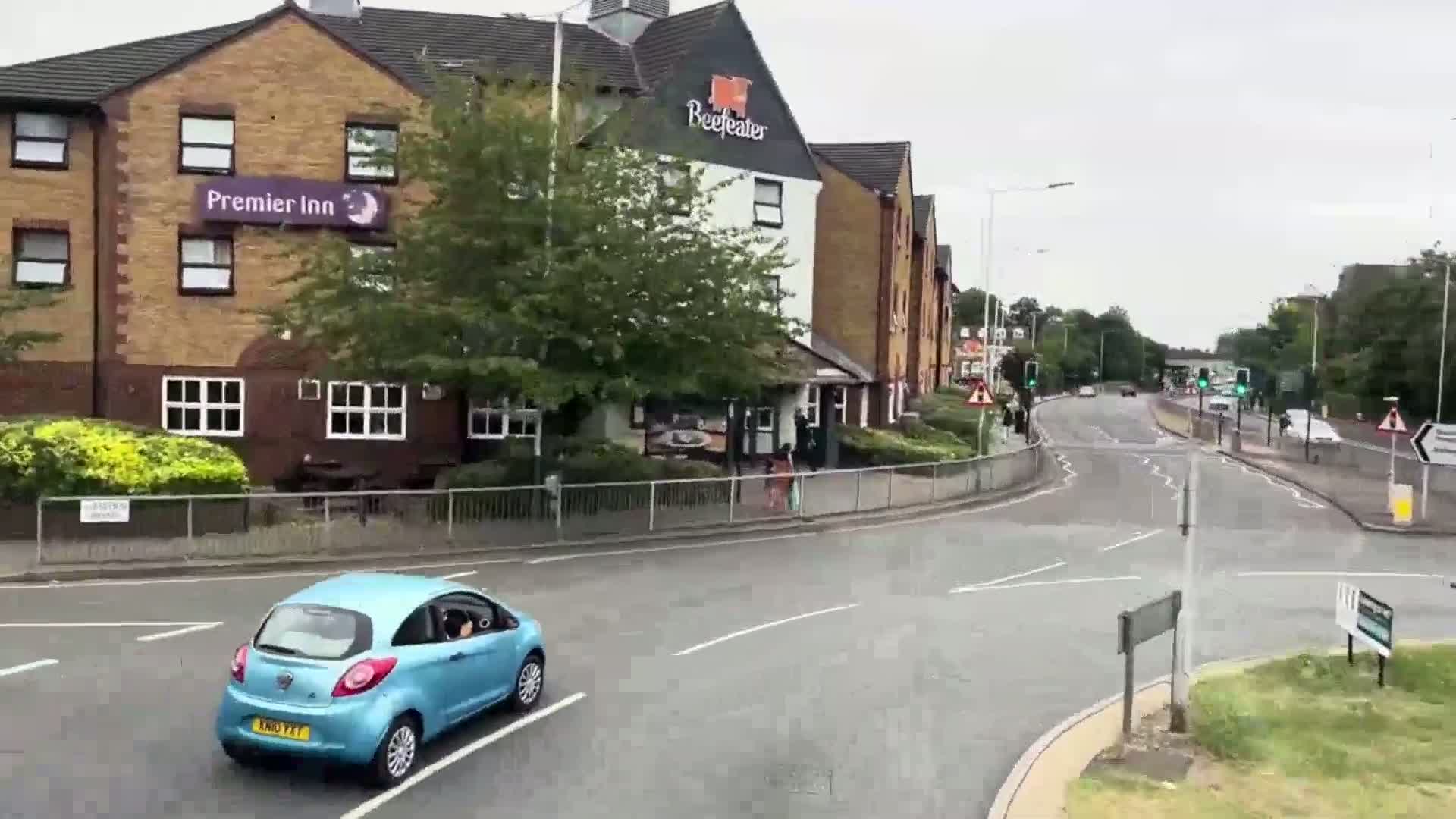 A light blue car drives past a Premier Inn and Beefeater restaurant on a wet road.