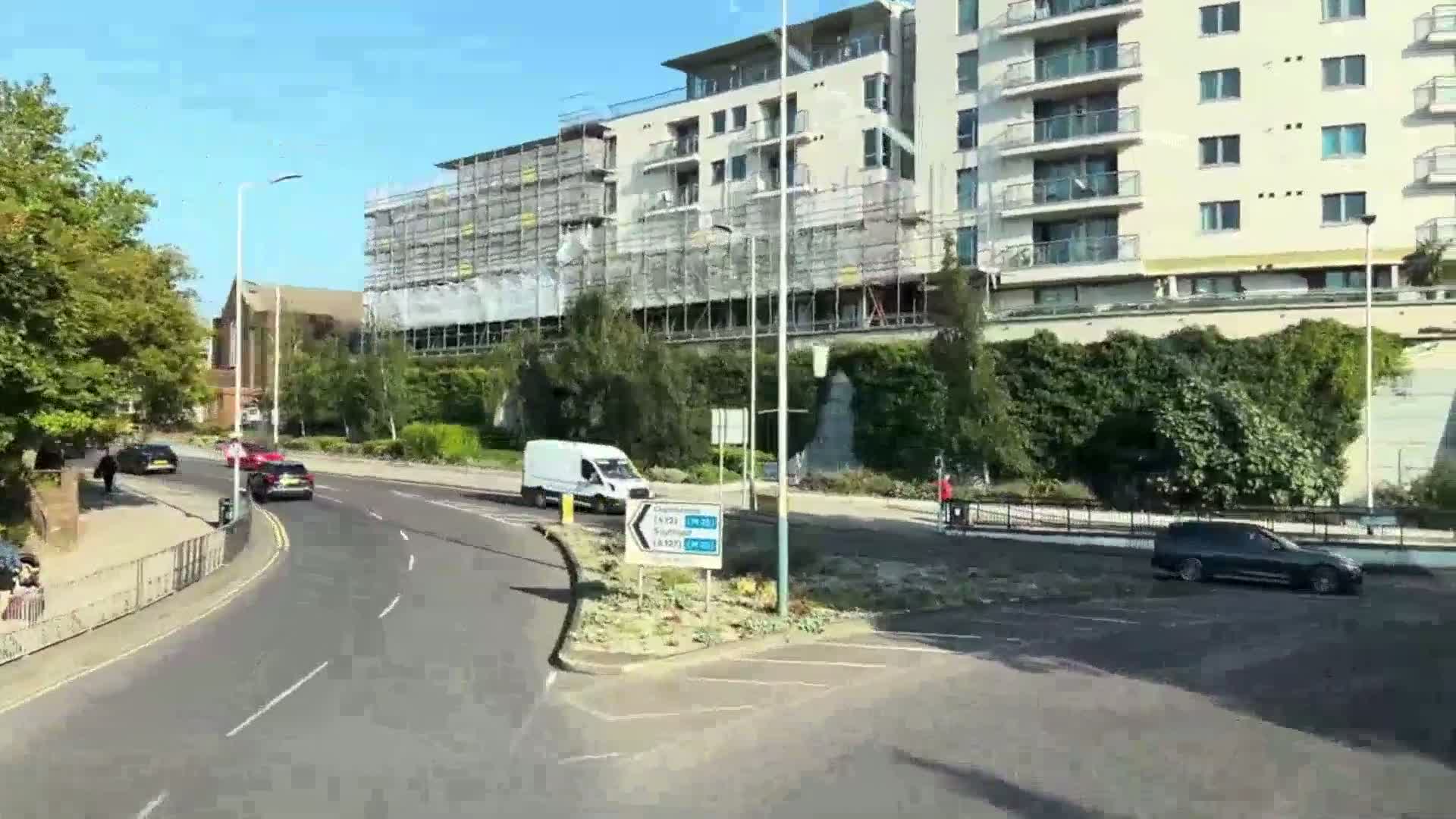 A sunny day shows a multi-story building under construction next to a roadway with several cars and a van.