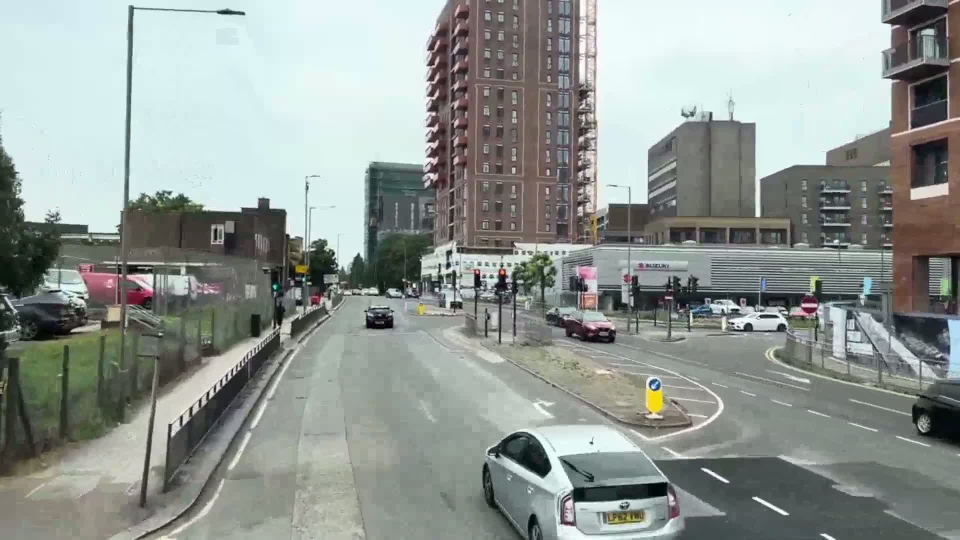 A city street scene on an overcast day shows several cars driving on a road that curves to the right, passing in front of several multi-story buildings.