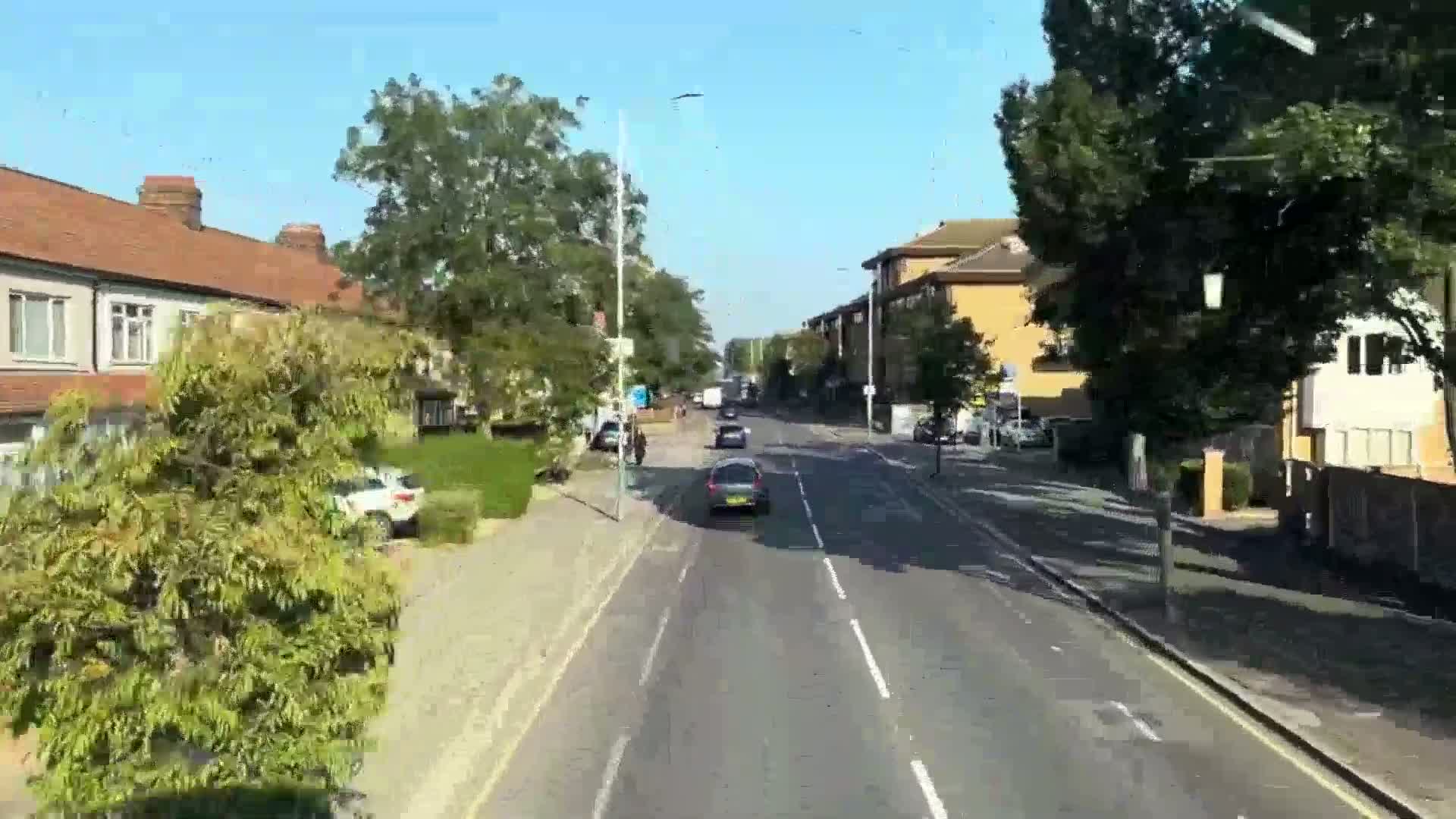 A sunny day reveals a residential street with houses and cars, viewed from a moving vehicle.