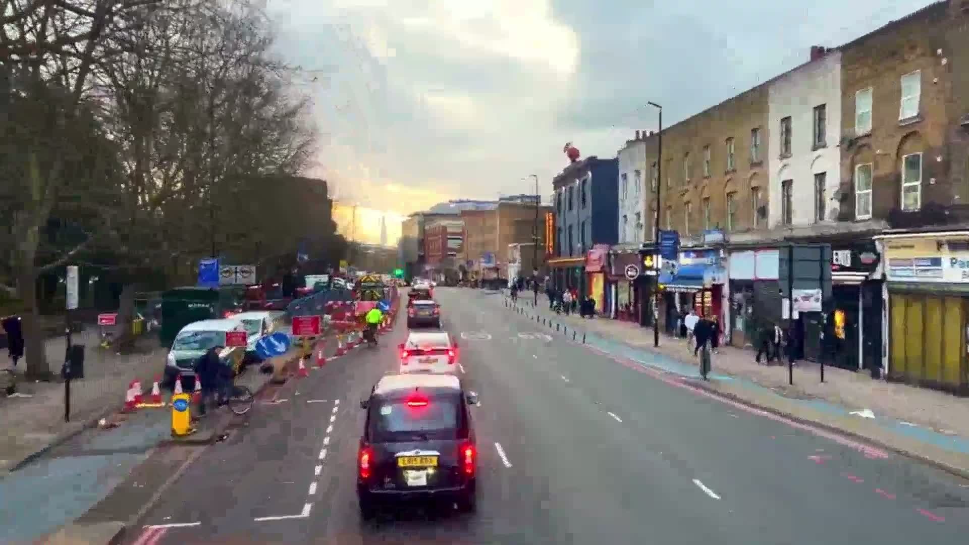 A city street with several cars and pedestrians, under a partly cloudy sky, has roadwork occurring on one side.