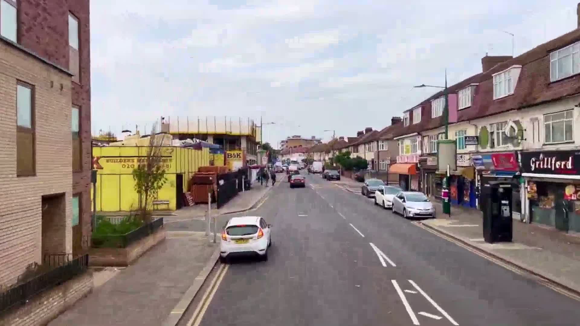 A street scene on an overcast day shows cars driving past shops and a building under construction.