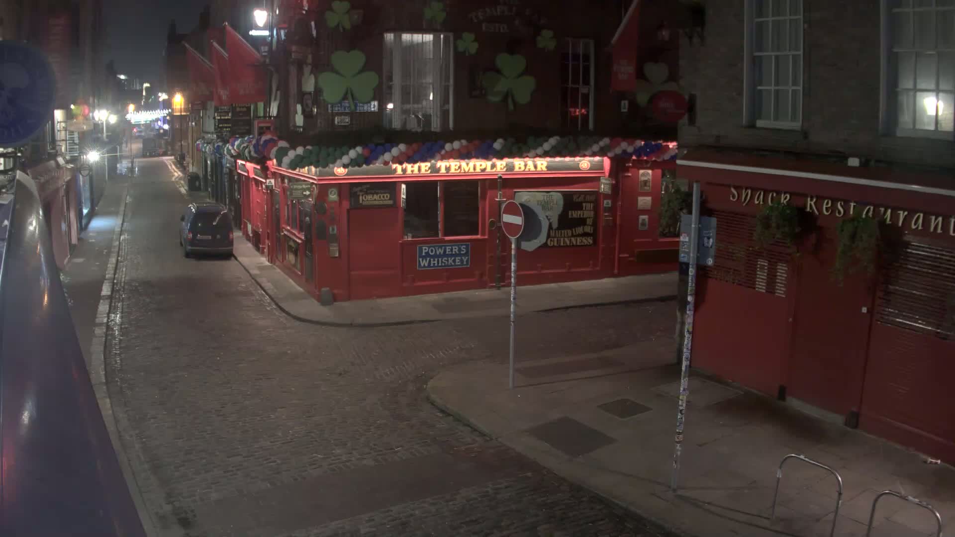 A dark, cobblestone street at night shows a red pub called "The Temple Bar" and a parked car.