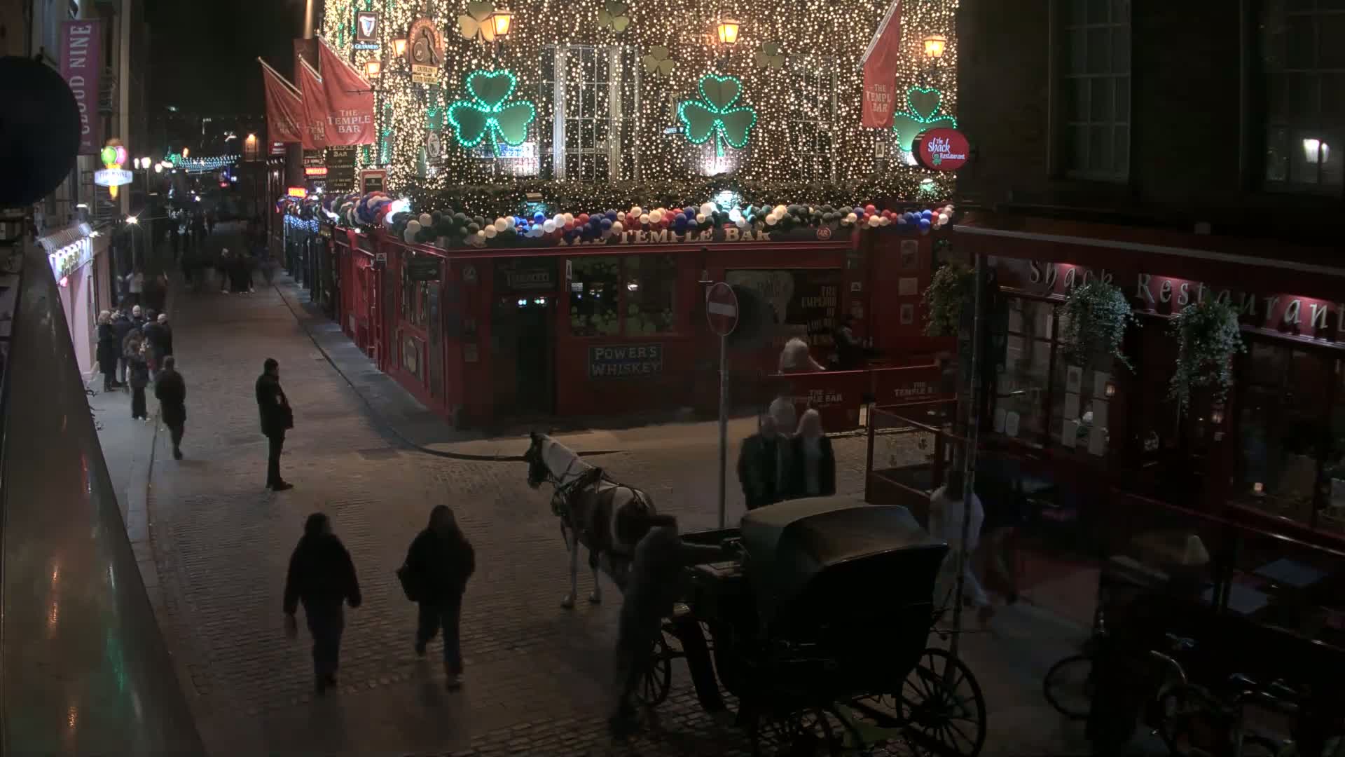 At night, a horse-drawn carriage waits on a cobblestone street lined with festively lit buildings and pedestrians.