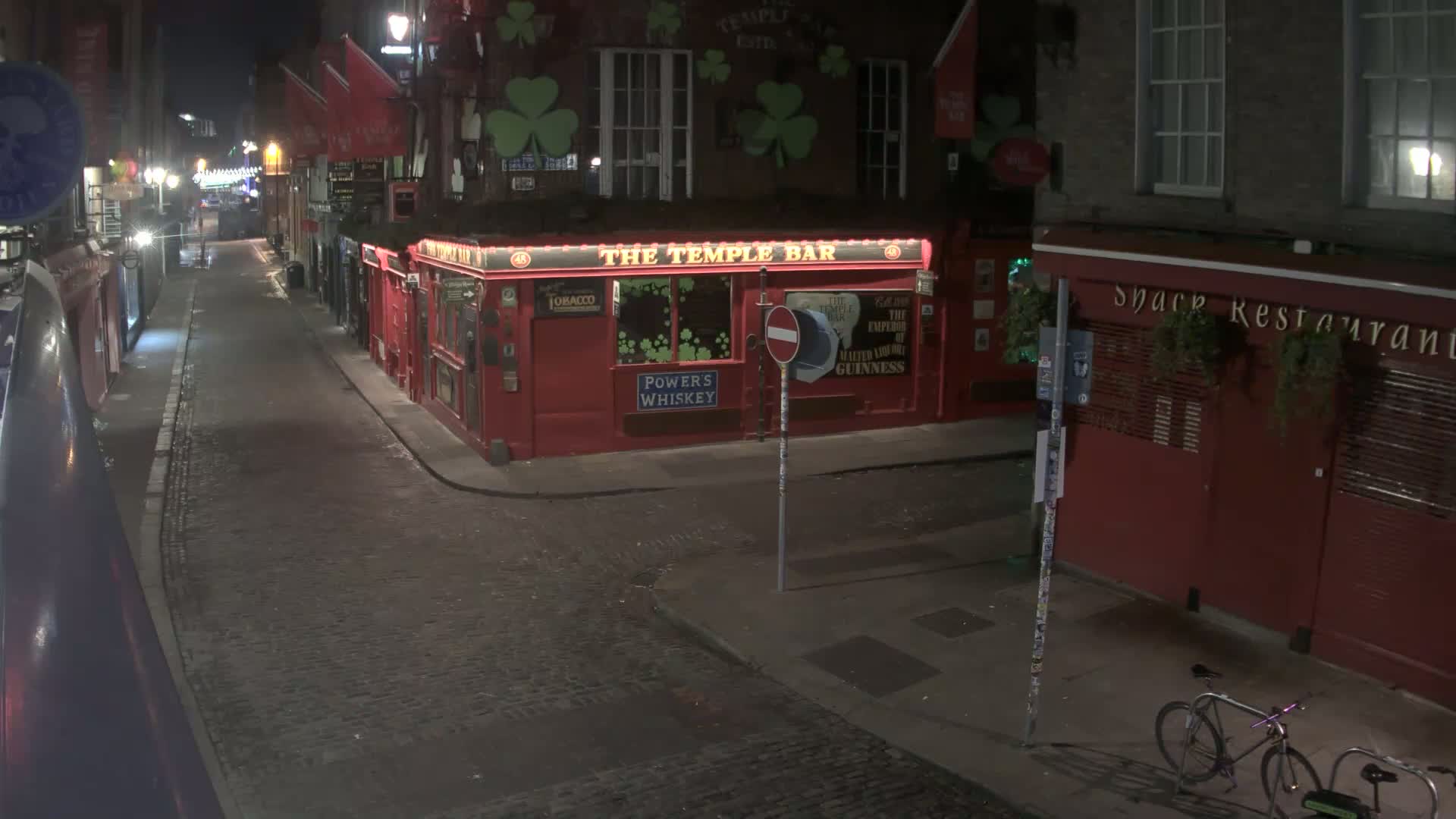 A cobblestone street at night, lined with red buildings including a pub, is nearly deserted except for a bicycle parked on the sidewalk.
