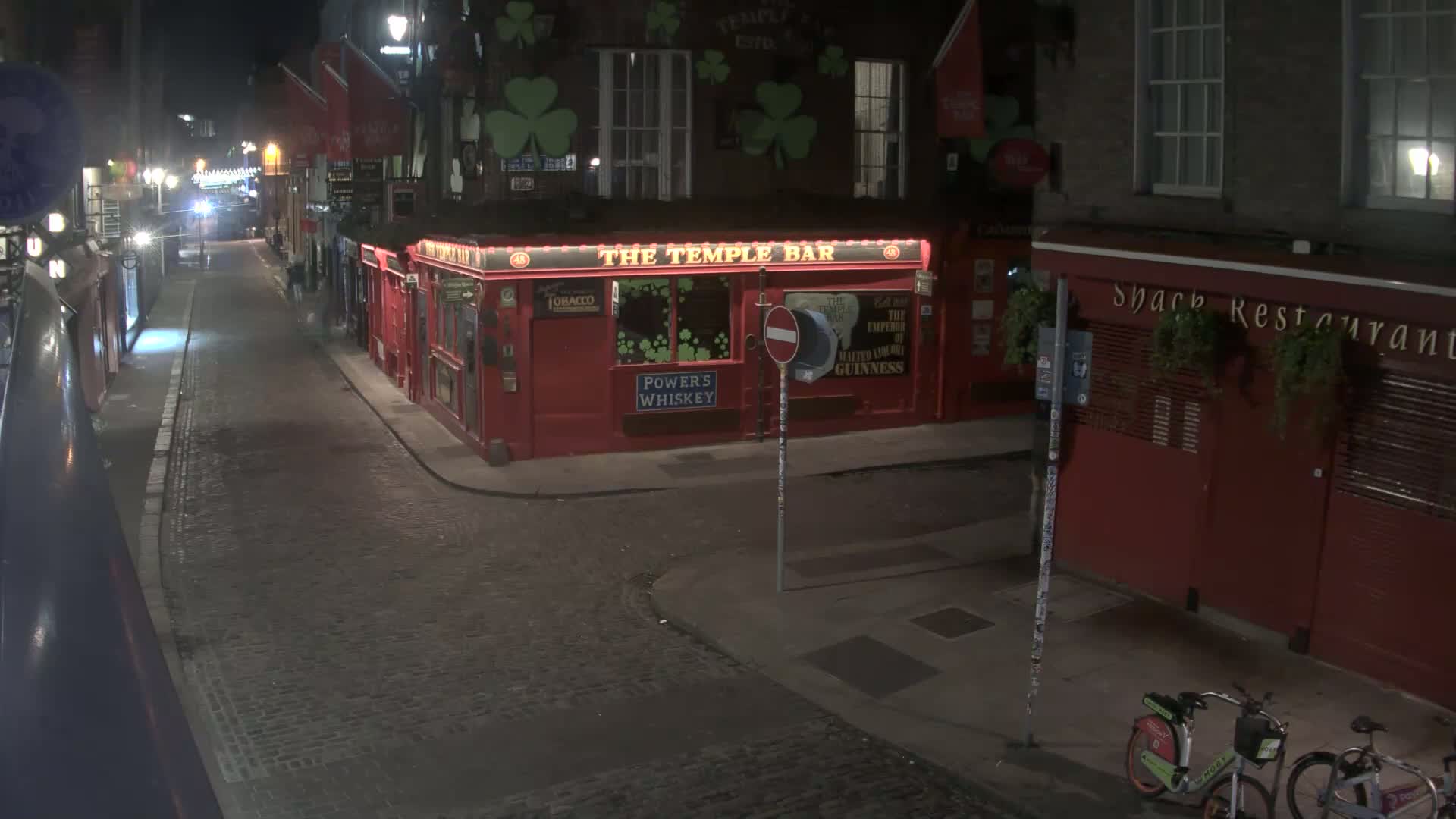 A nighttime view of a cobblestone street with red brick buildings, including a pub called "The Temple Bar," and two bicycles parked against one of the buildings.