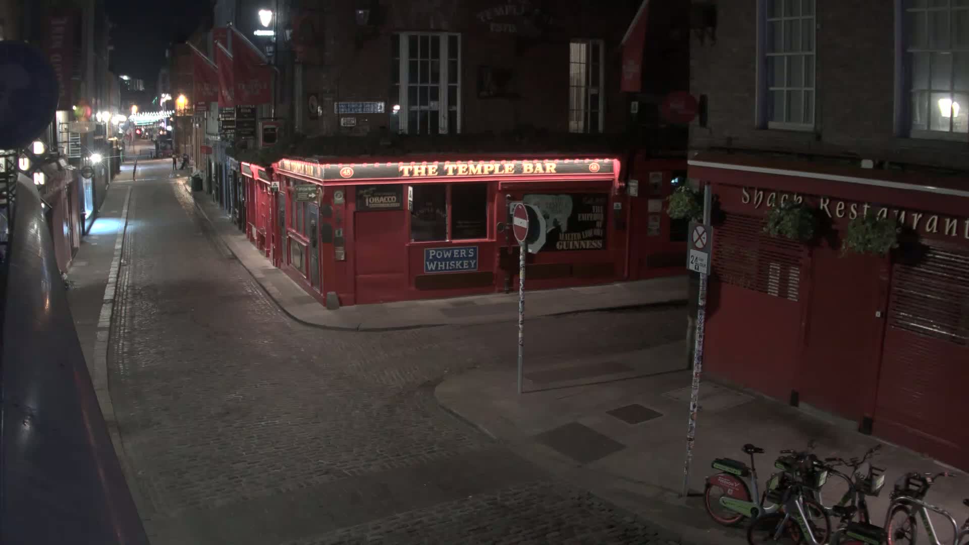 A nearly deserted cobblestone street at night, lined with red buildings, including a pub and restaurant, is dimly lit by streetlights.
