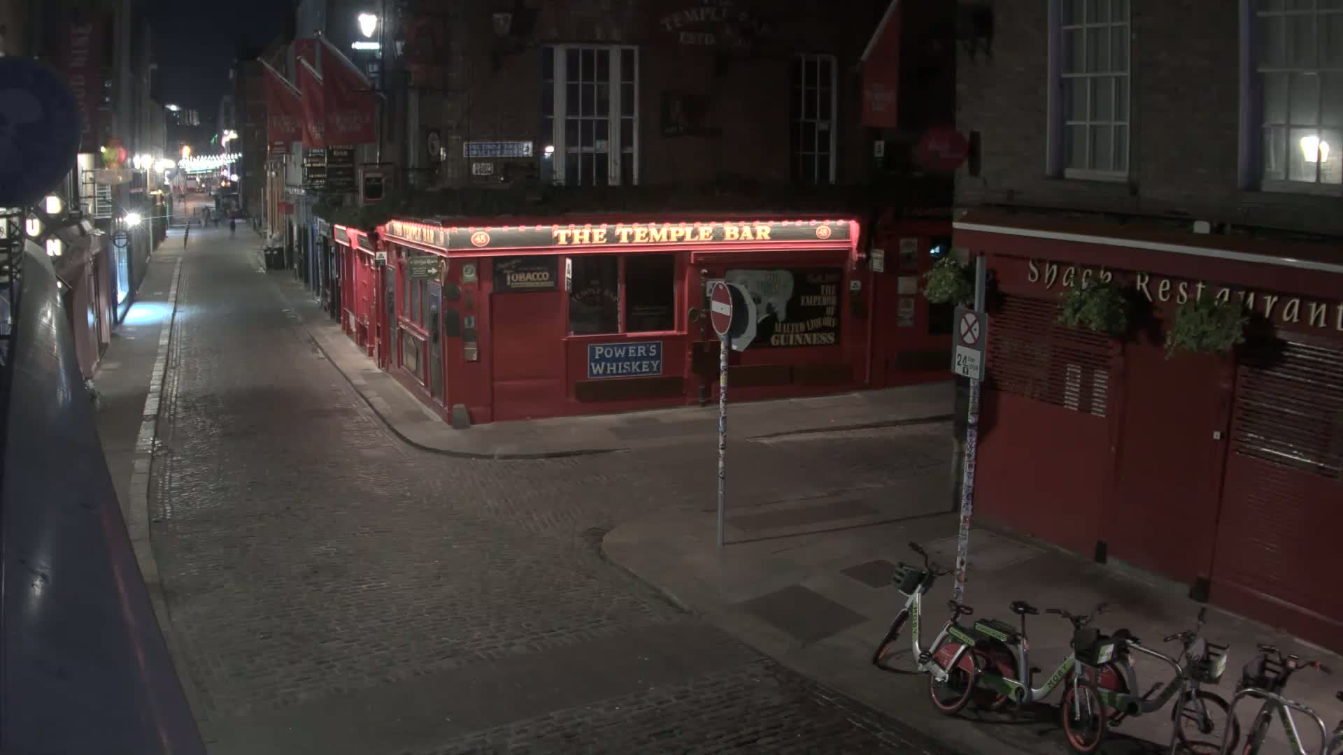 A quiet, cobblestone street at night, lined with red buildings, including a pub and a restaurant, with several bicycles parked along the sidewalk.
