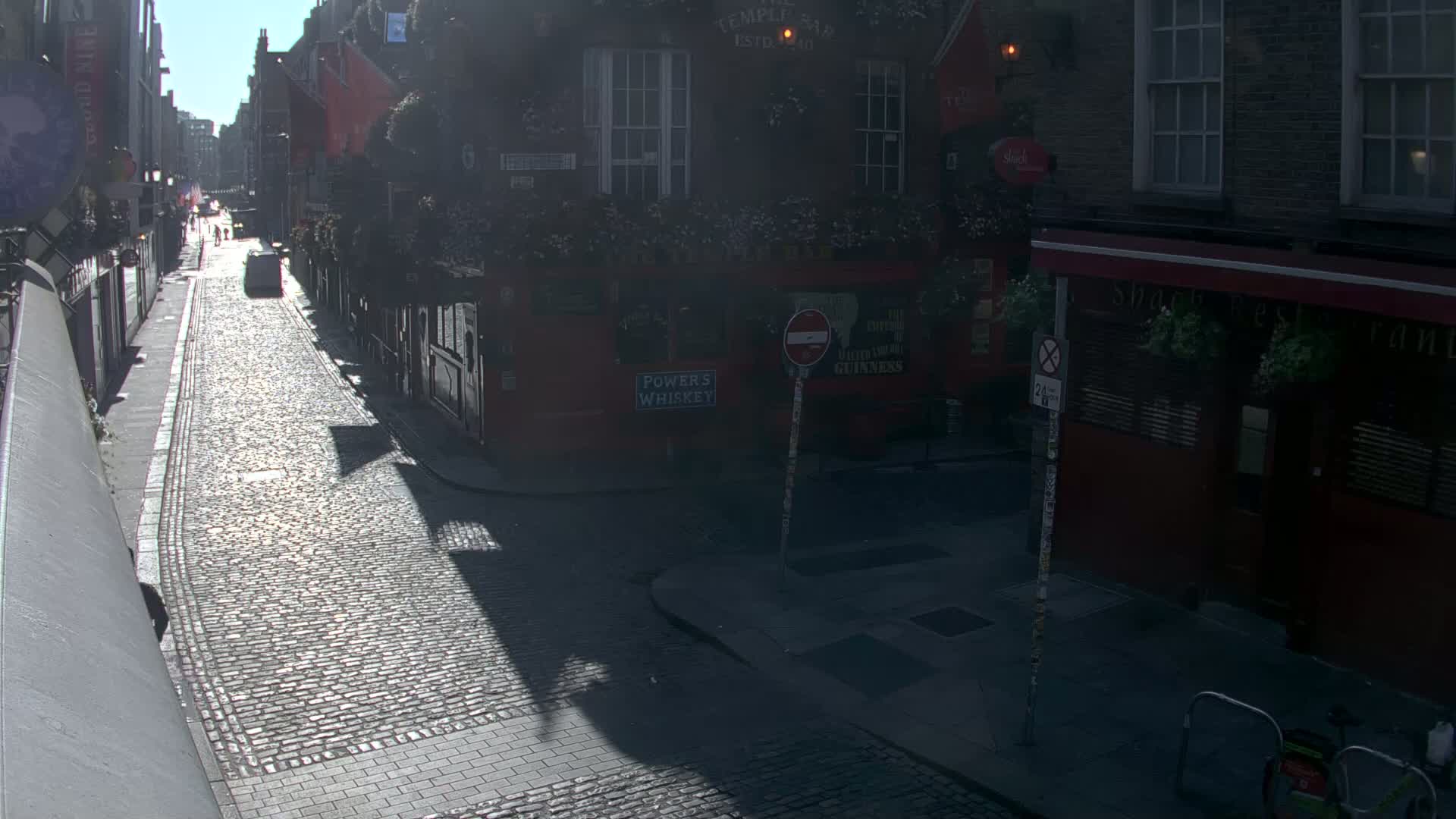 A sunny day on a cobblestone street between brick buildings, with shadows cast across the road.