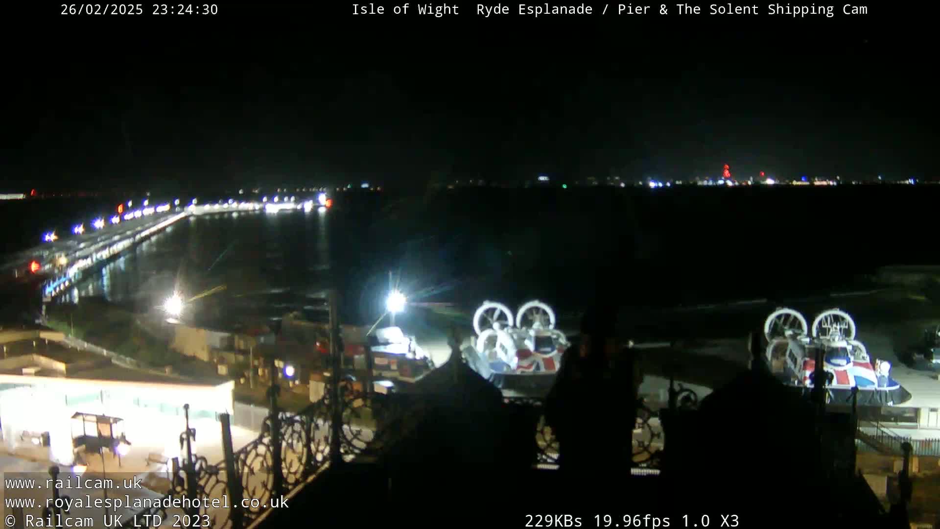 A nighttime view of a pier and waterfront area with two hovercrafts parked on the shore, illuminated by lights.