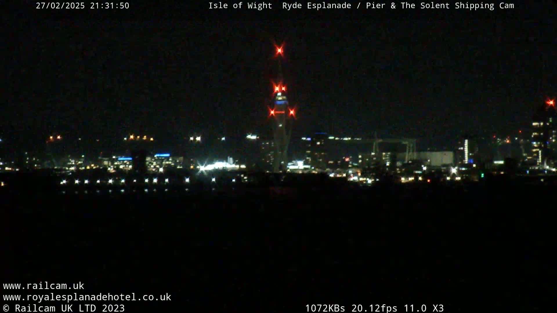 A nighttime long shot of a city skyline illuminated by lights, with a tall tower prominently featured in the center.