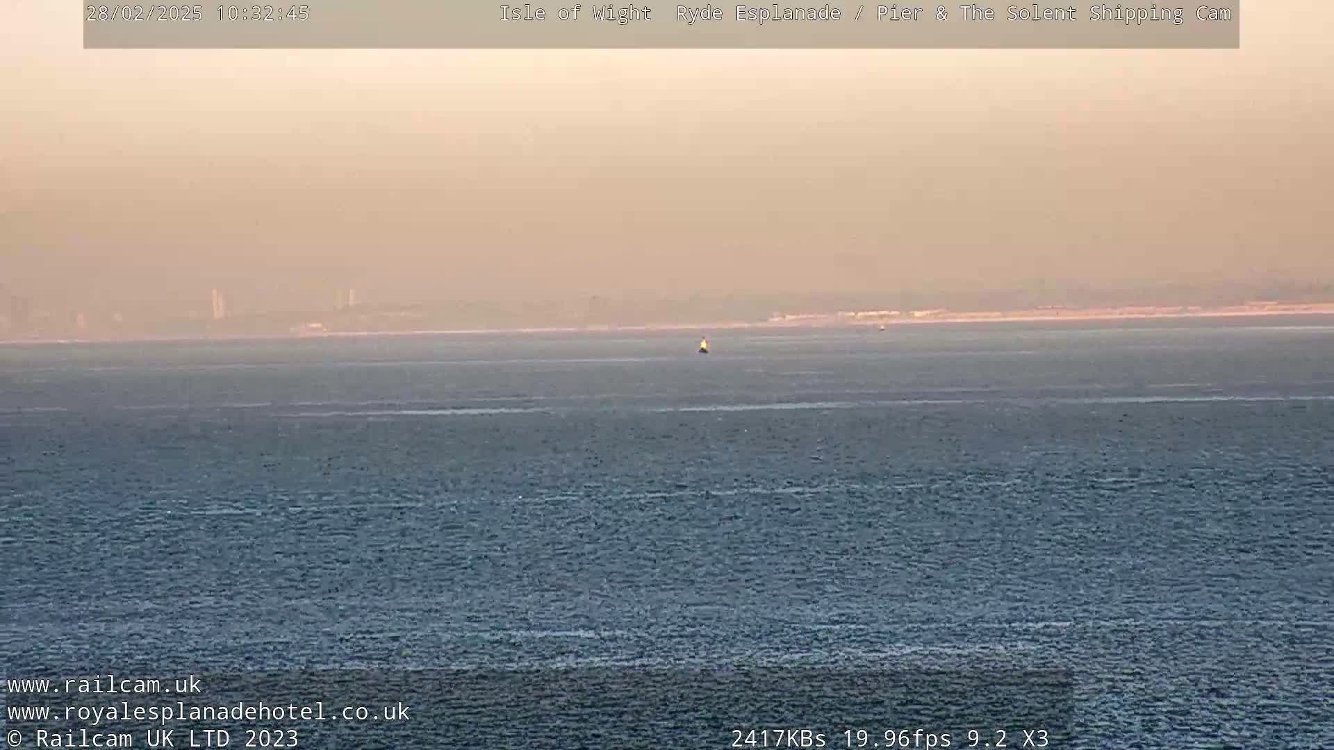 A hazy, calm body of water stretches to a distant shoreline under a pale, orange-tinged sky.