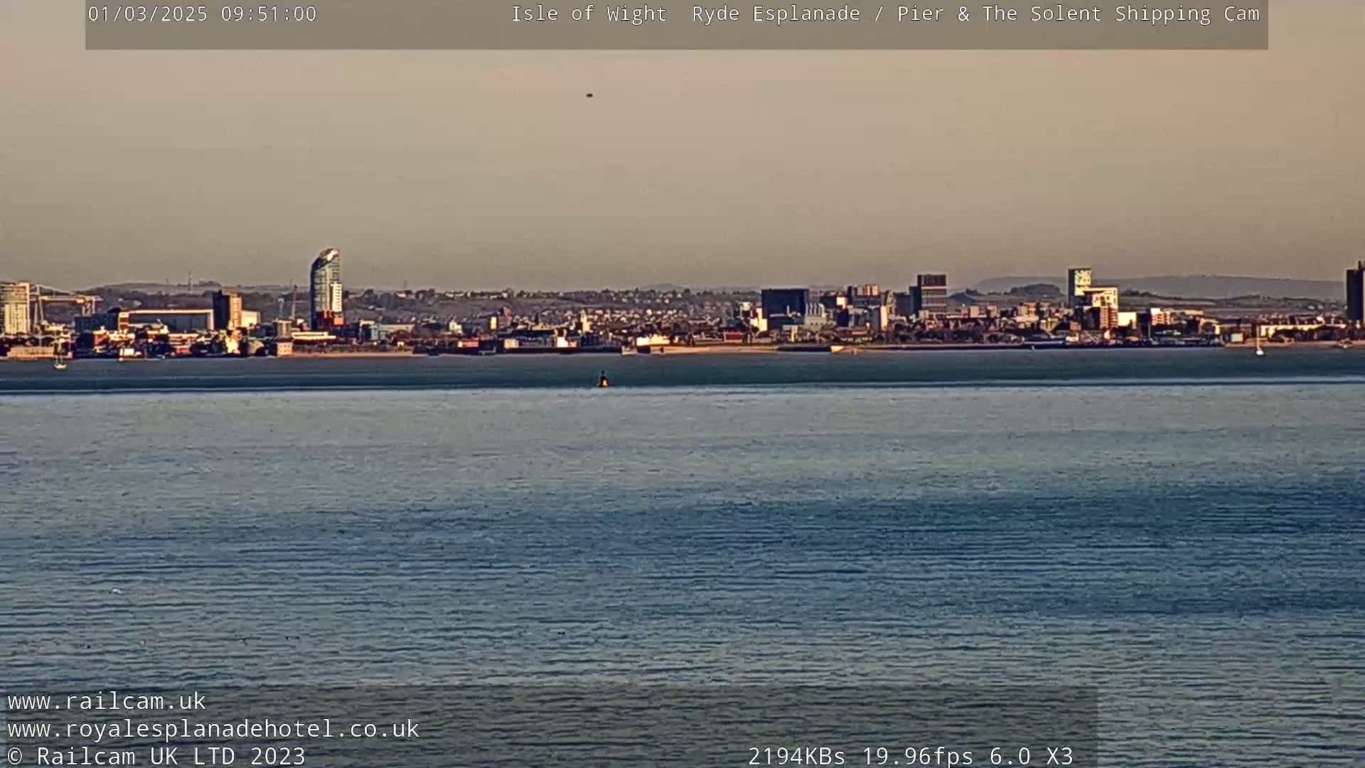 A calm body of water shows a distant cityscape under a hazy sky.