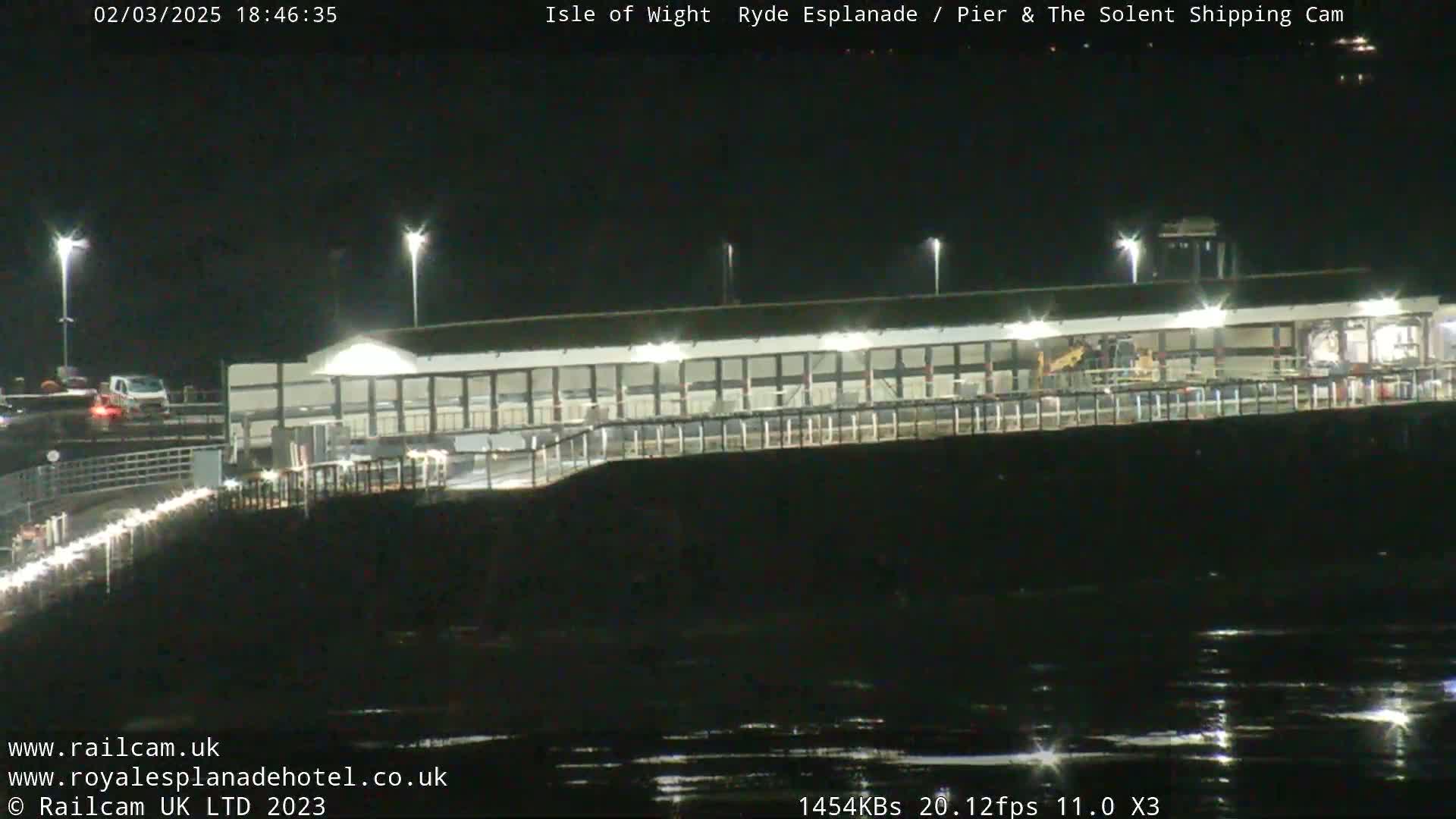 A nighttime, low-light view of a pier illuminated by lights, reflecting on dark water.