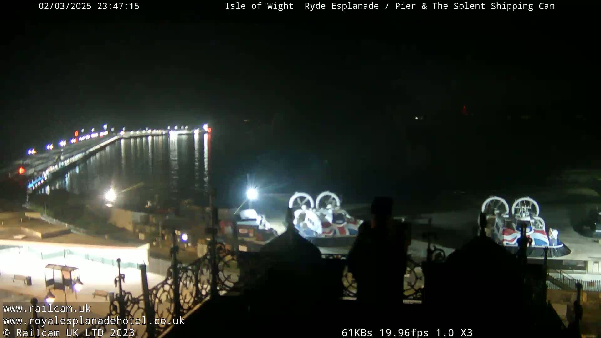 A nighttime view of a pier and harbor with a hovercraft on the shore, under clear skies.