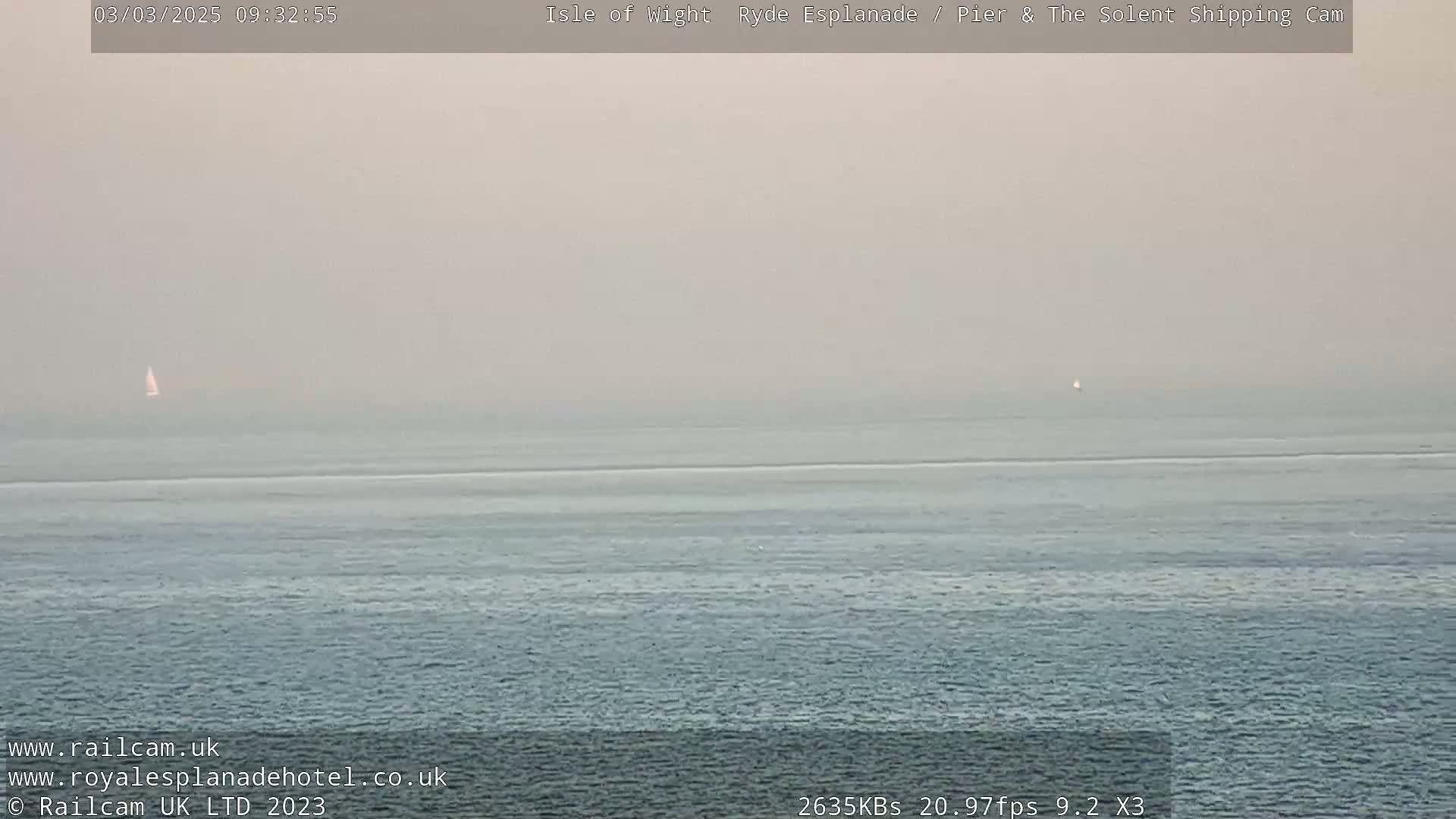 A hazy, calm ocean scene shows two distant sailboats.