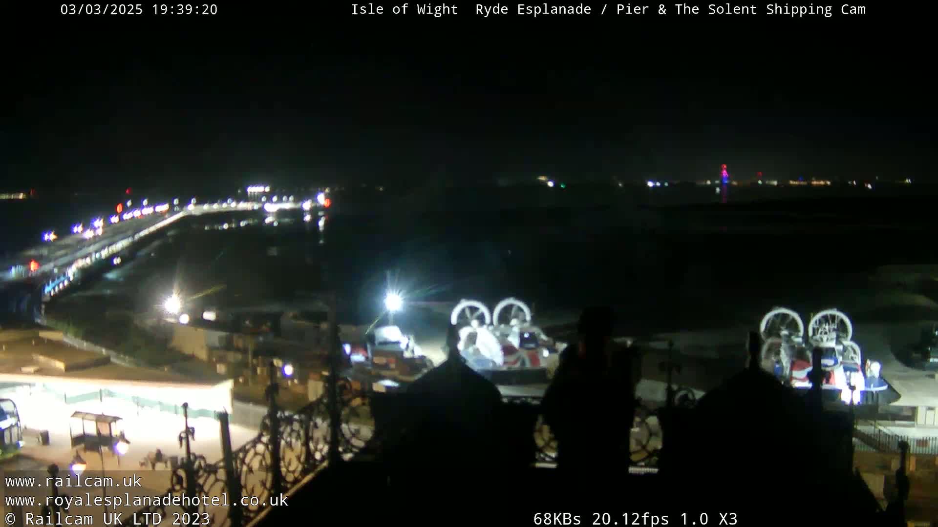A nighttime, long shot of a waterfront area with a hovercraft and lights illuminating the scene.