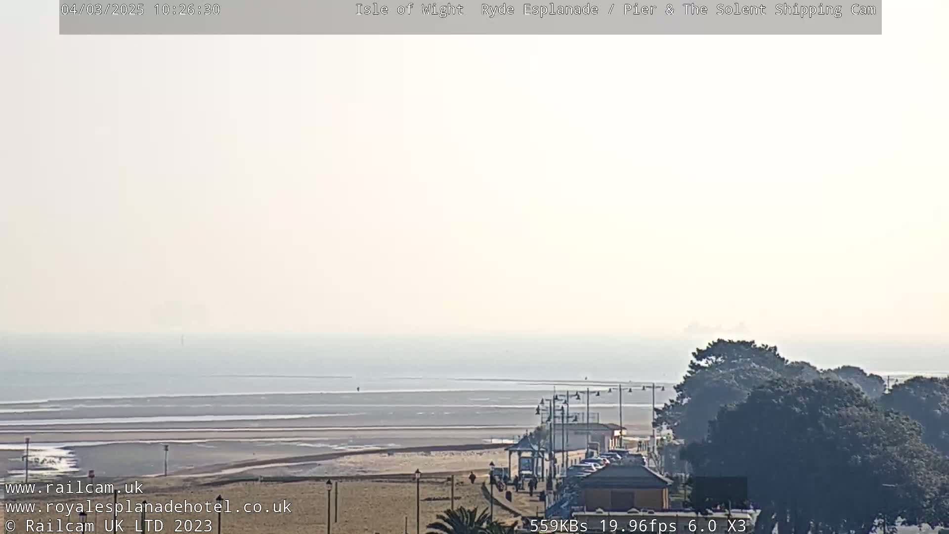 A hazy, sunny day overlooking a beach, ocean, and seaside town with some people walking along the shore.