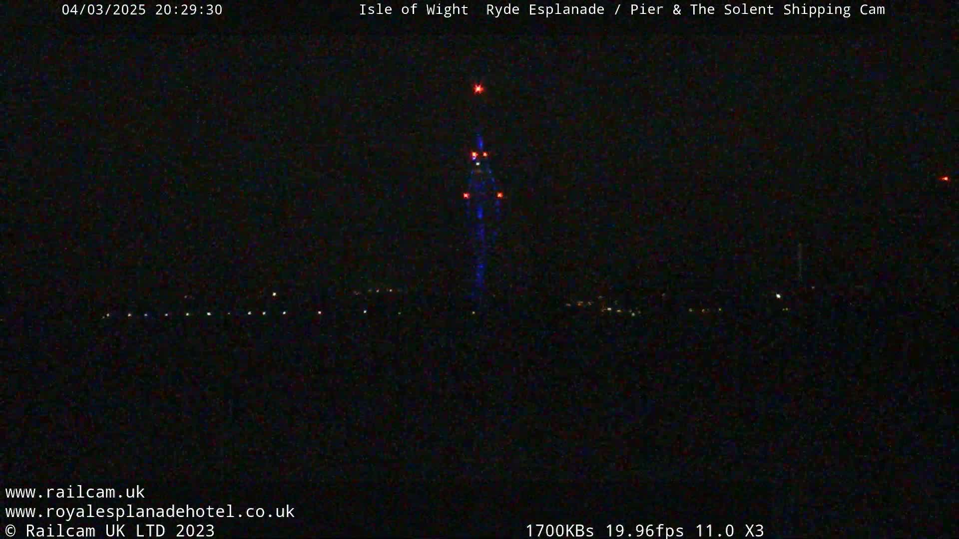 A tall structure with lights is visible against a dark, nighttime sky, with a few other distant lights in the lower portion of the image.