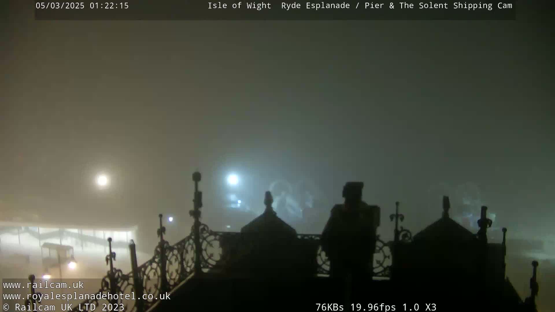 A foggy nighttime scene shows a view from an elevated position overlooking a dimly lit area with silhouettes of people and ornate architectural details.