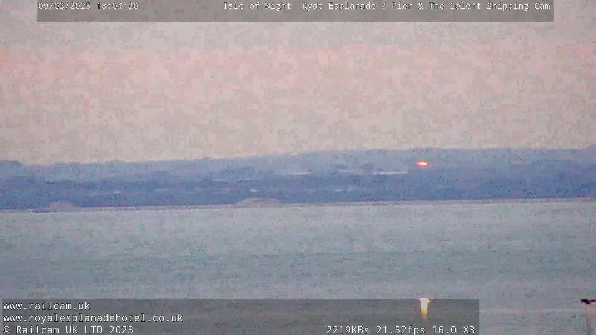 A calm body of water stretches to a hazy, distant shoreline under a pale, pinkish-grey sky.
