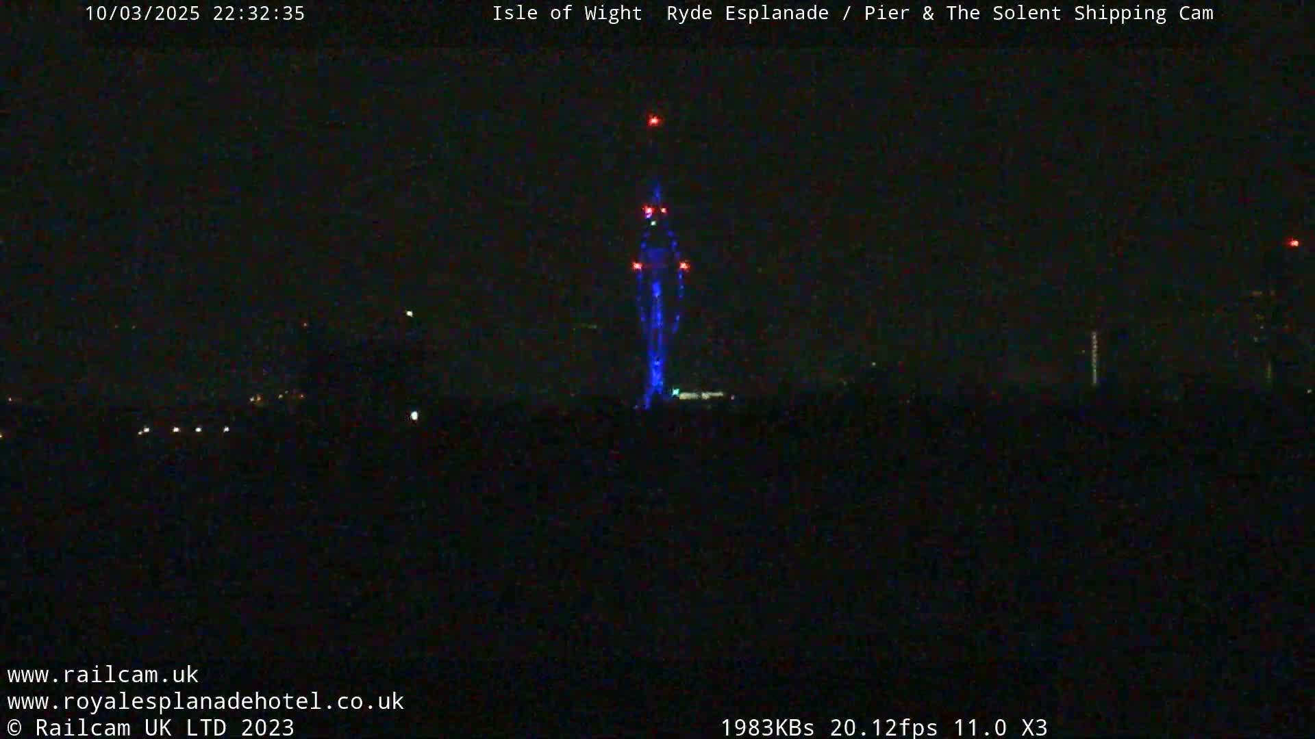 A tall, slender structure illuminated in blue is visible against a dark, nighttime sky.
