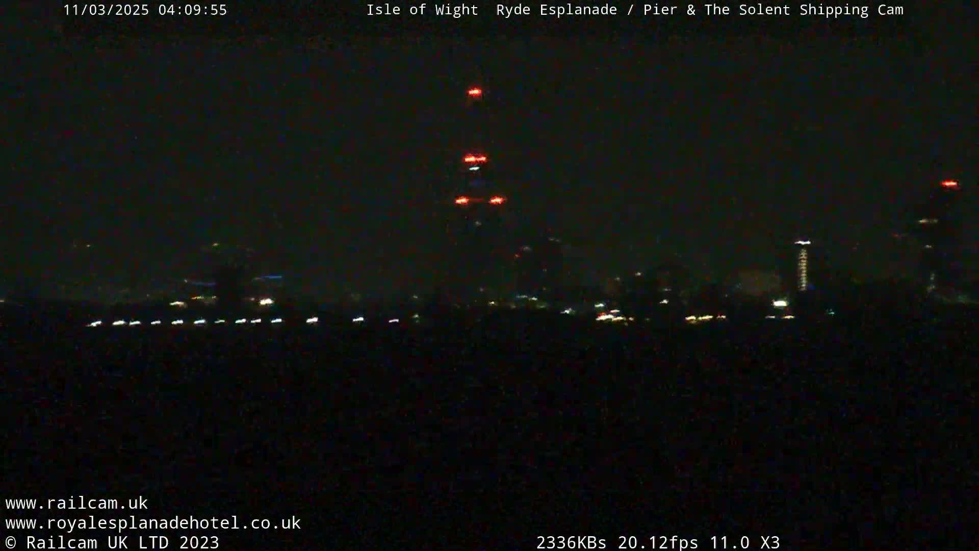 A nighttime, dark view of a city skyline with a few lights visible across a body of water.