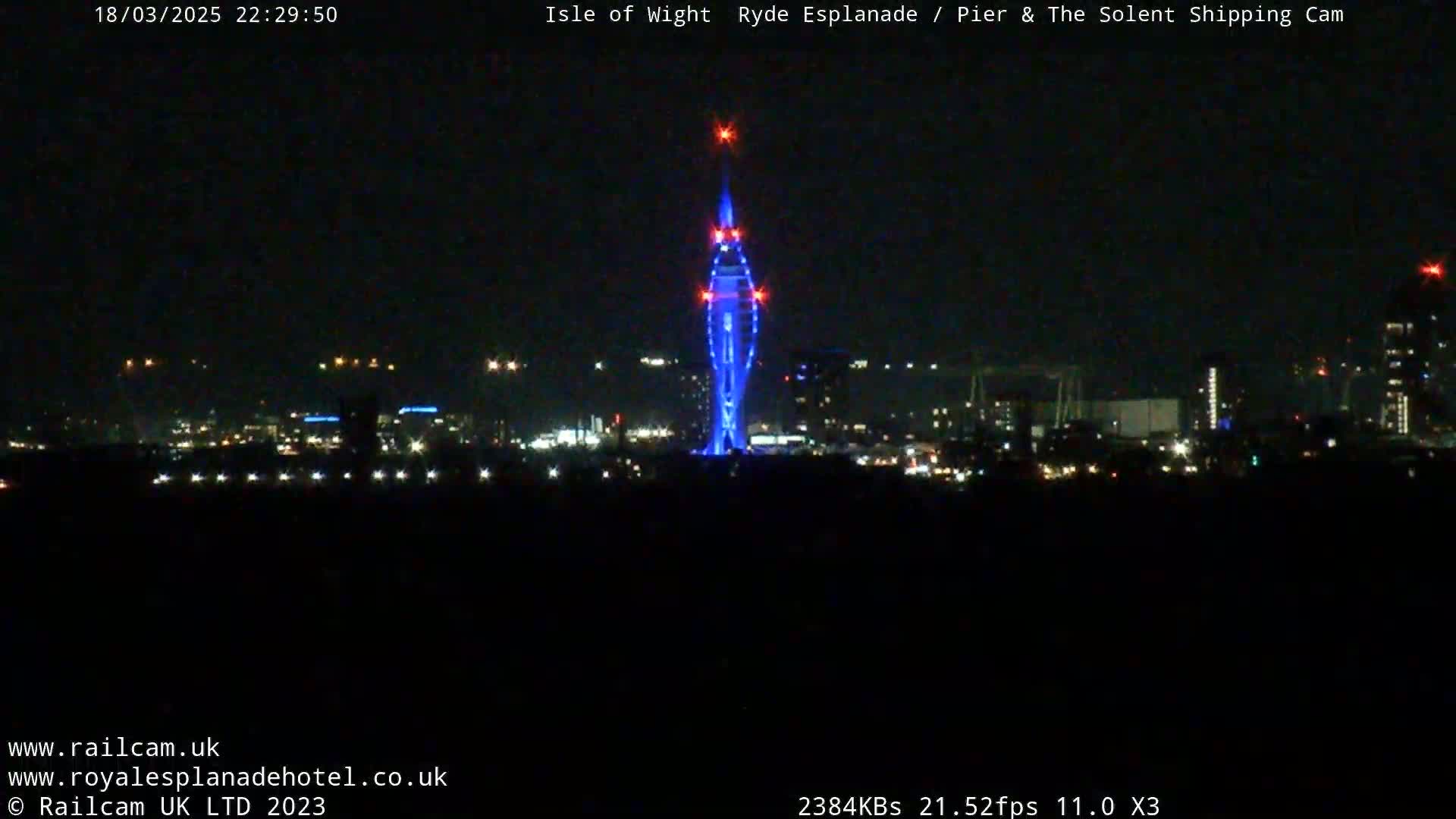 A tall, illuminated tower stands out against a dark, nighttime cityscape.