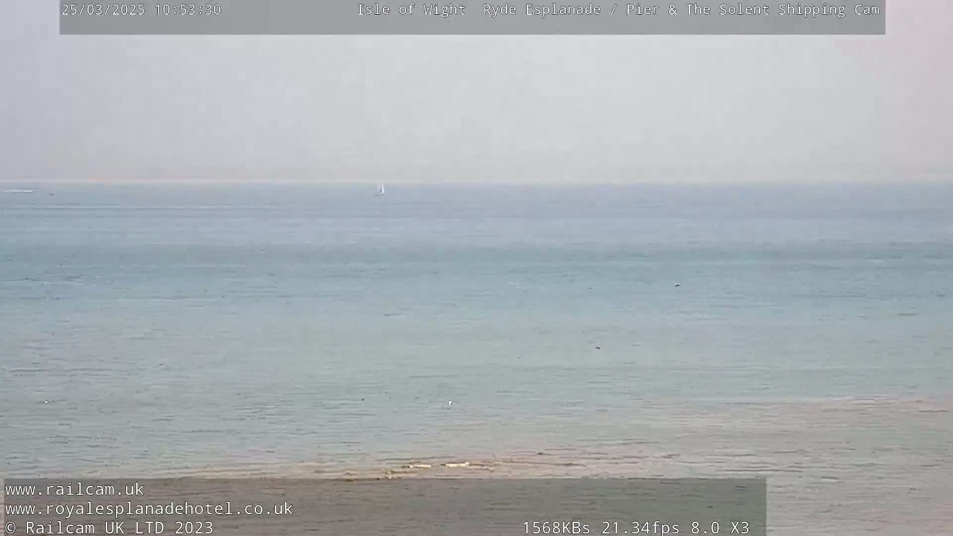 A calm, hazy ocean scene shows a distant sailboat and a small shoreline.