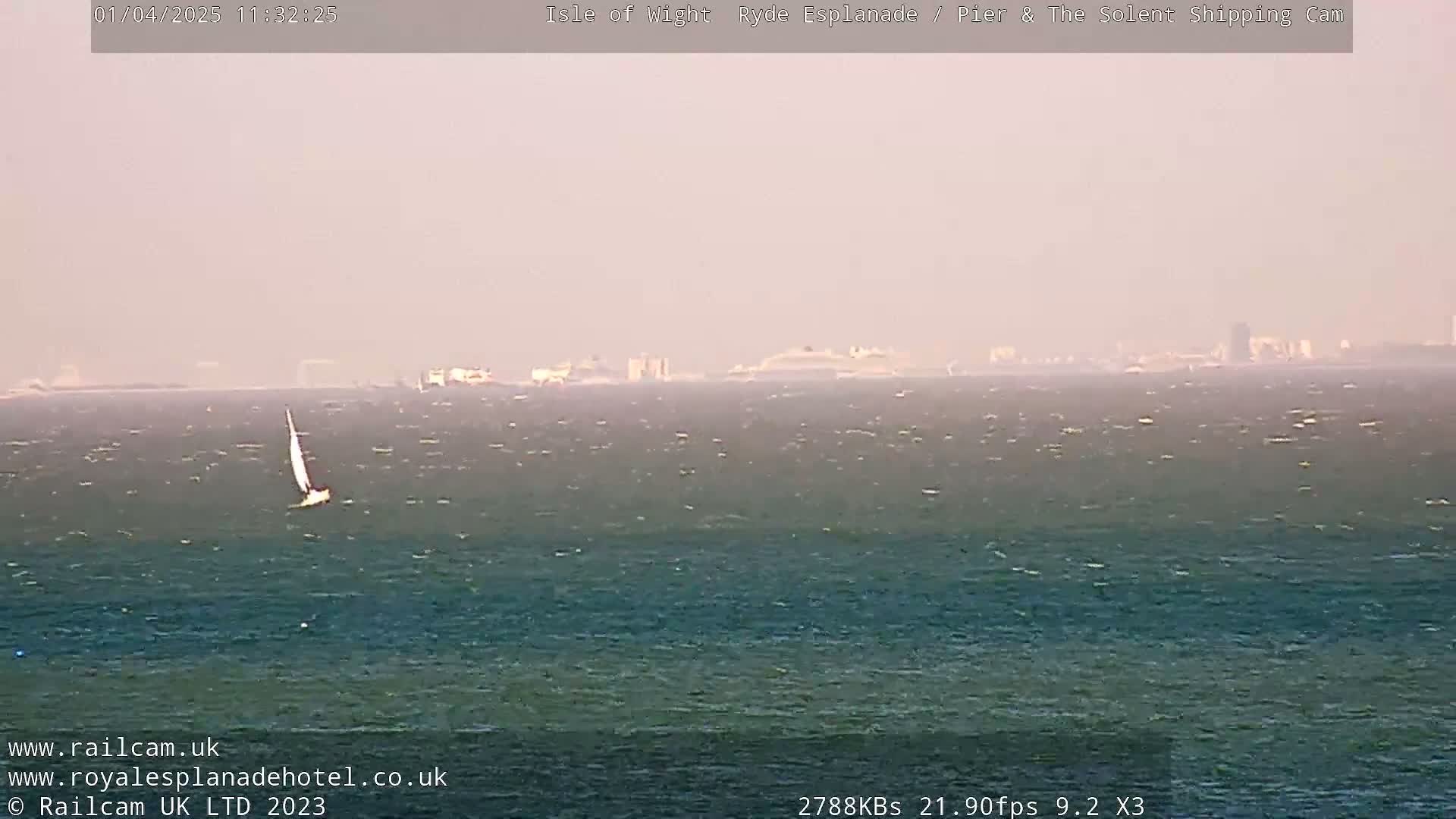 A sailboat is visible on a choppy sea under a hazy sky with a distant shoreline.