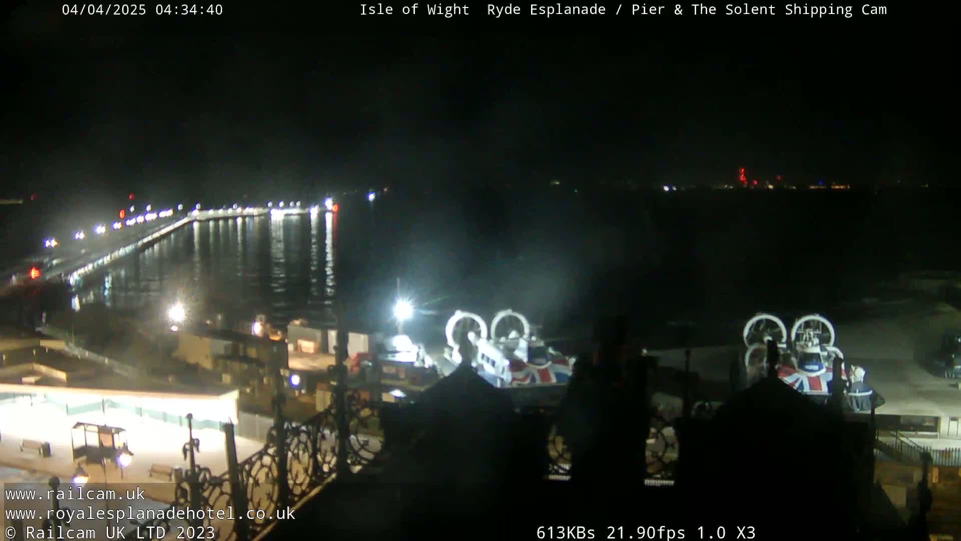 A nighttime view of a pier and body of water with two hovercrafts docked near a building, under a clear, dark sky.