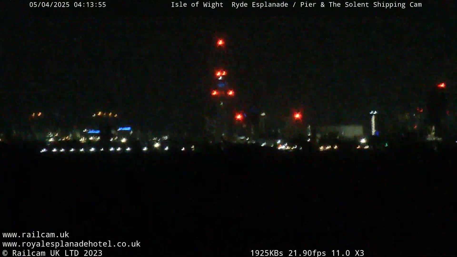 A nighttime, long-range view of a city skyline with various lights, including several bright red lights atop a tall structure.