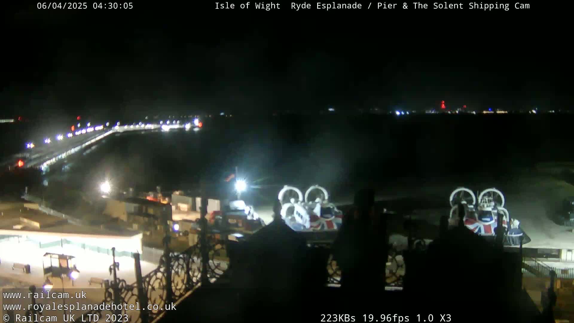 A nighttime, wide shot shows a hovercraft at a pier, with lights visible along a waterfront road and in the distance.