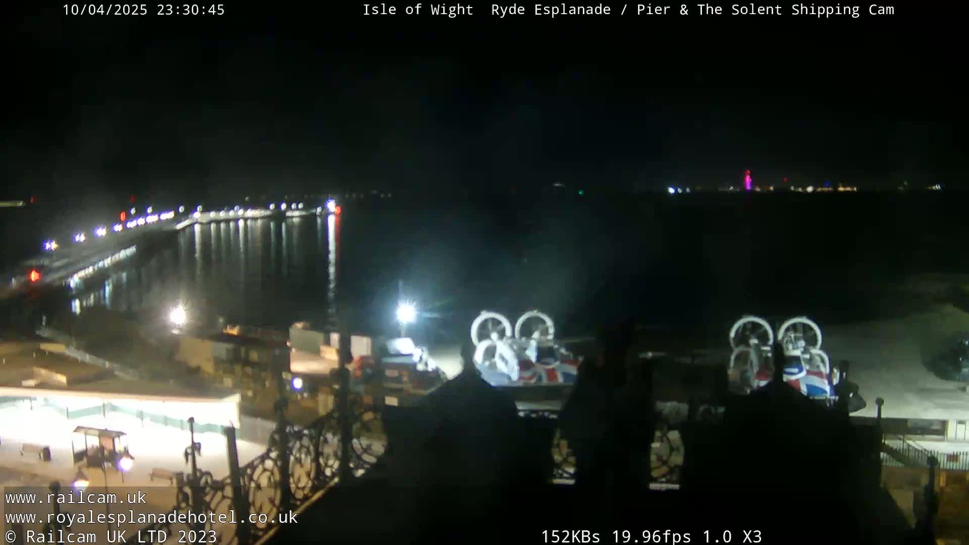 A nighttime view of a pier and calm water, with two hovercrafts parked on the shore under dark, clear skies.