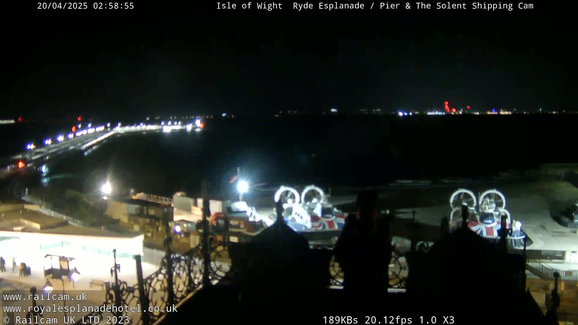 A nighttime view of a pier and body of water, with a hovercraft visible in the foreground and lights illuminating the scene.