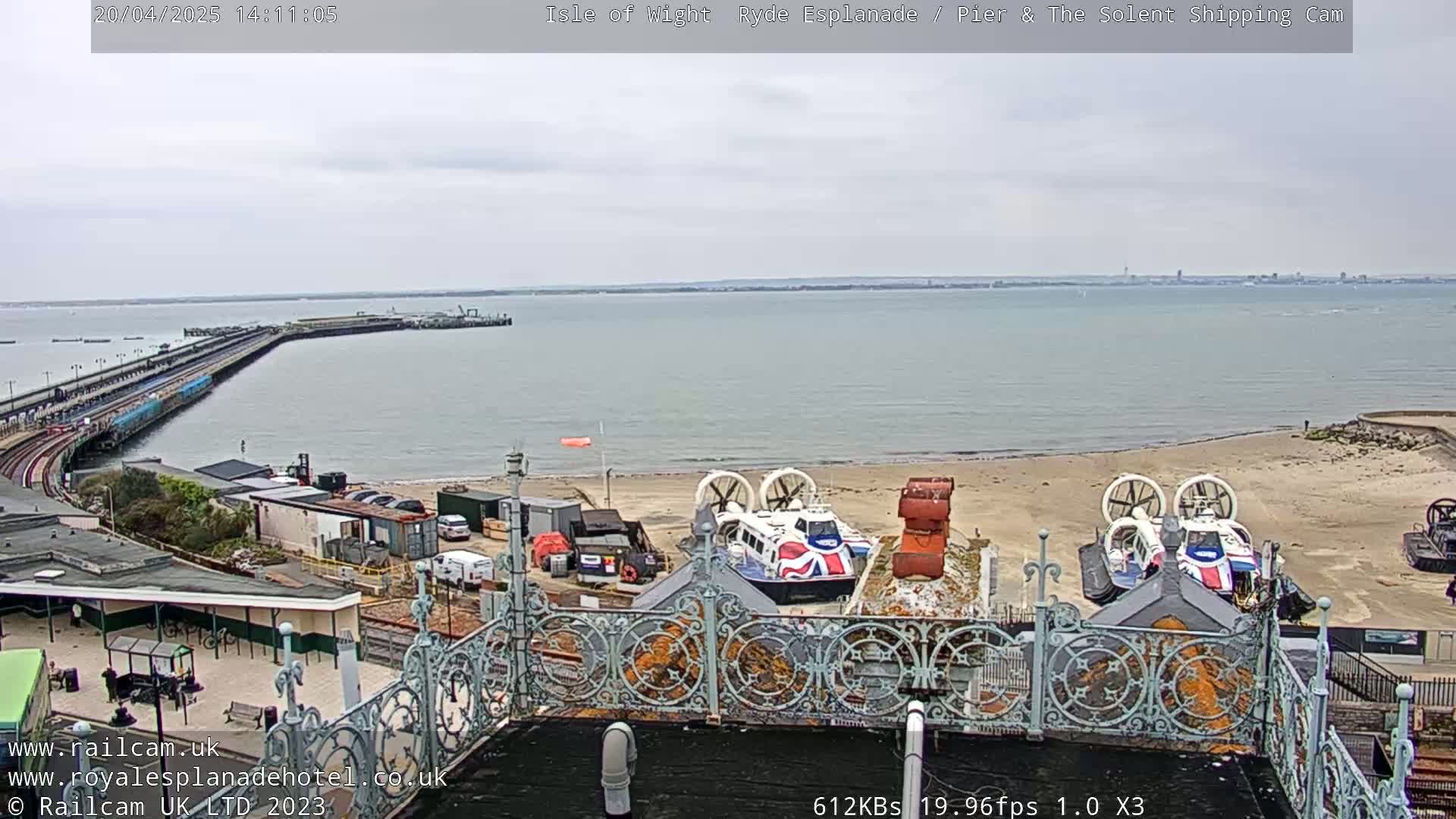 A beach with a hovercraft, a pier extending into a calm body of water under an overcast sky.