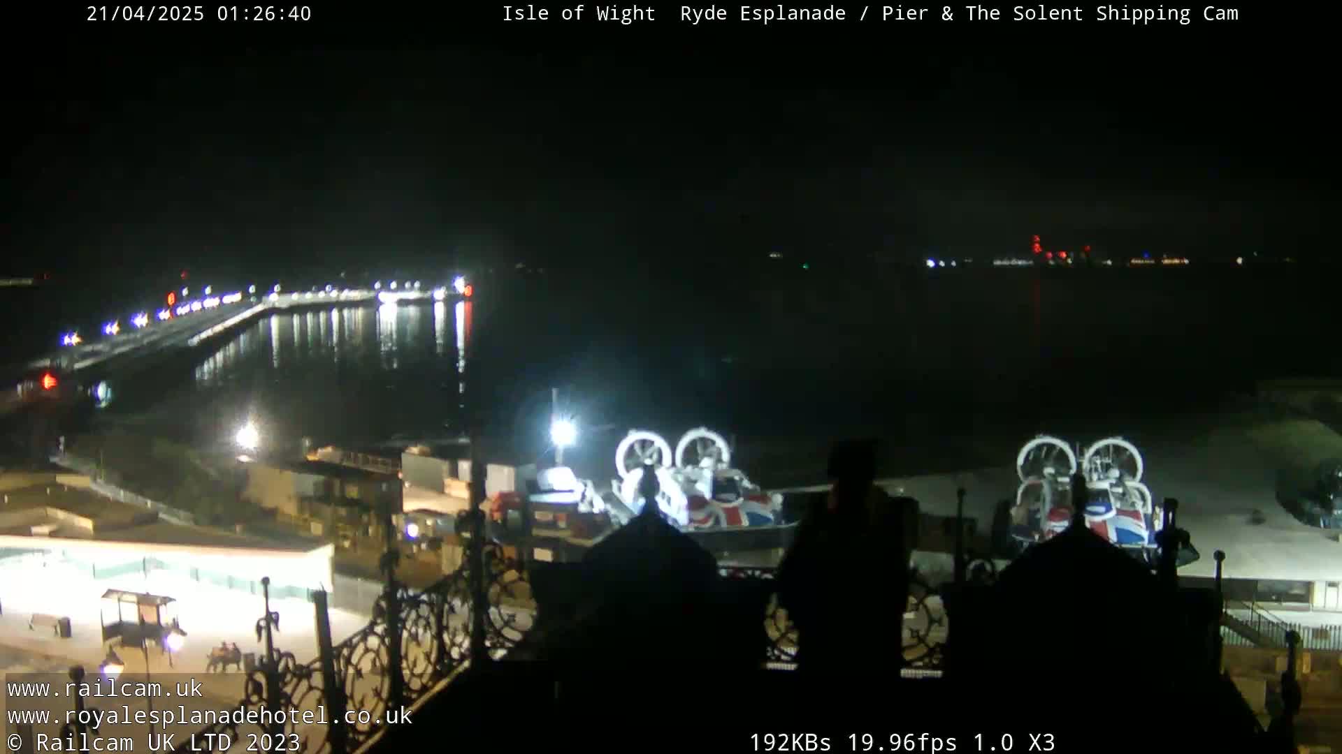 A nighttime view of a body of water with a pier and two hovercrafts docked, under a clear, dark sky.