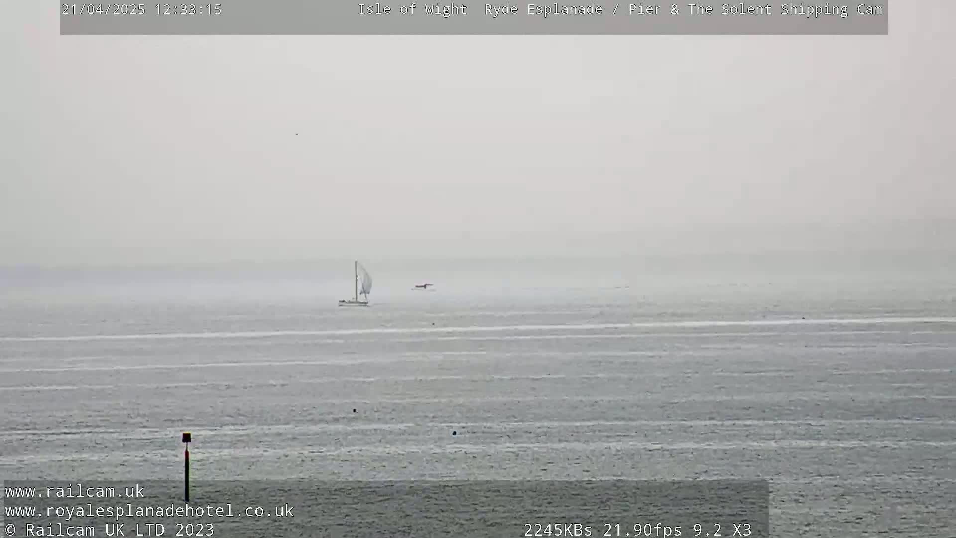 A hazy, overcast day shows a sailboat and a smaller vessel on calm water.