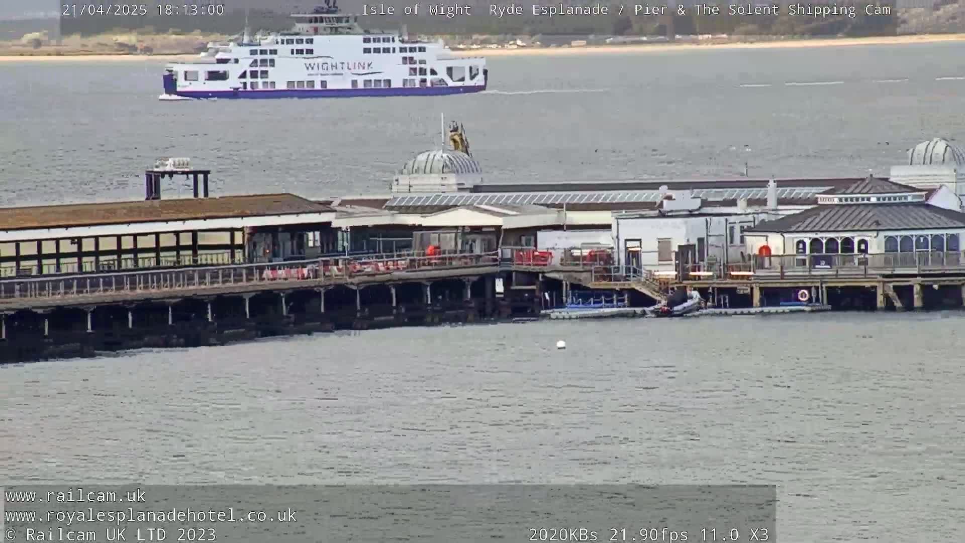 A ferry passes by a pier with buildings on it in calm water.
