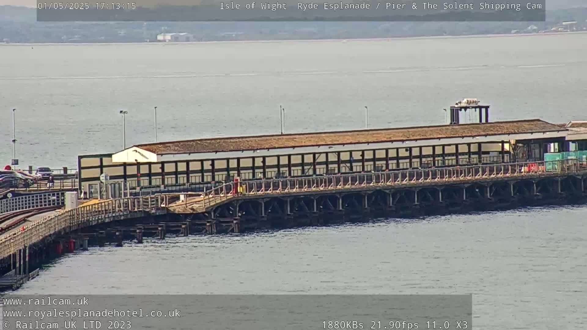 A long pier with a building extends over calm, gray water.