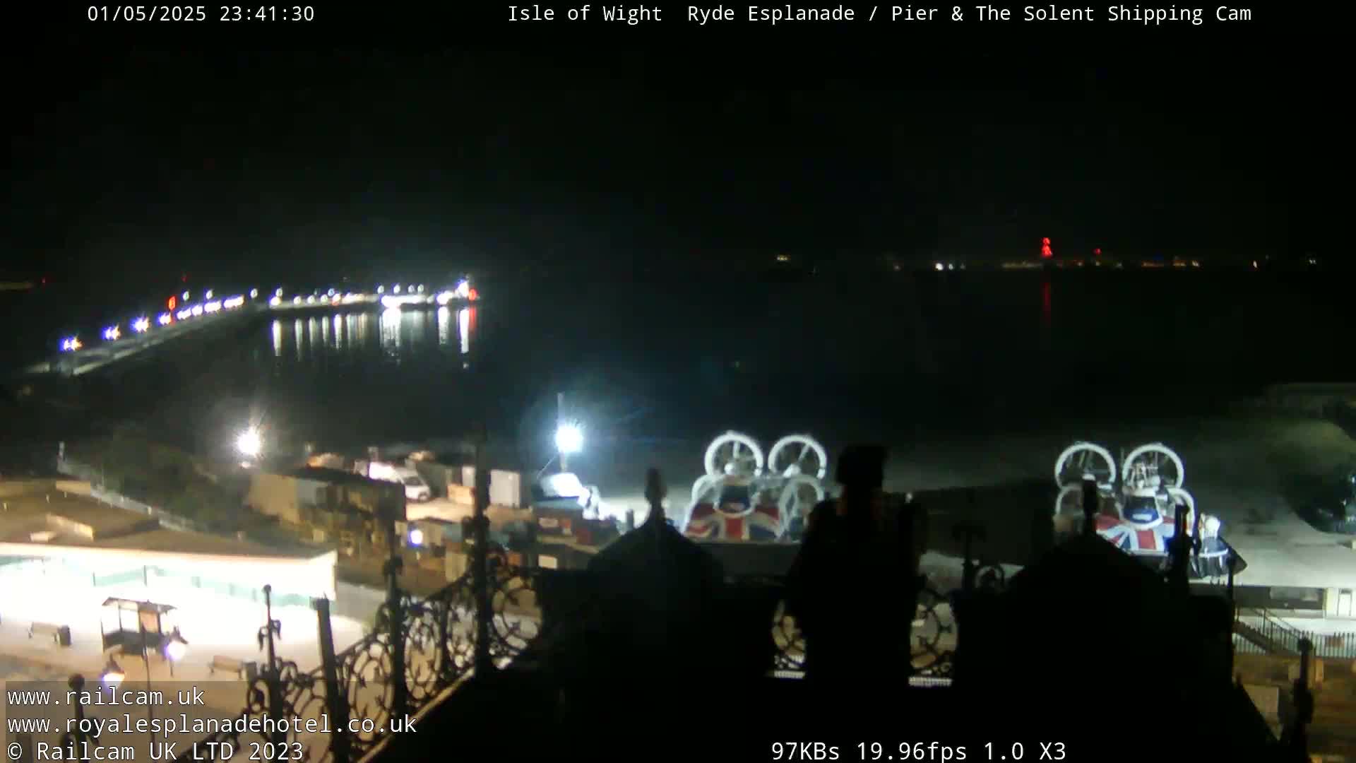 A nighttime view of a waterfront area with a hovercraft and lights reflecting on dark water.