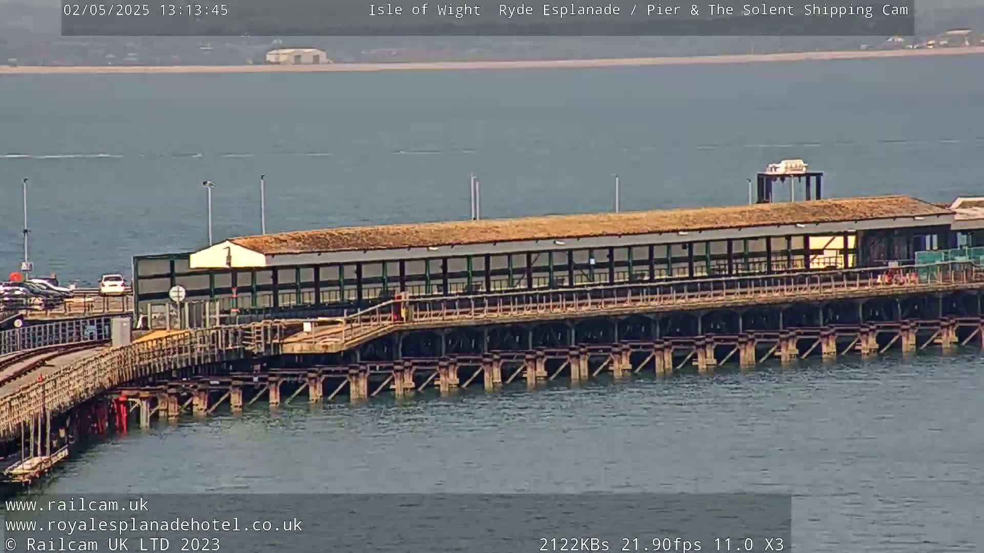 A long pier extends over calm, gray-blue water under a bright, sunny sky.