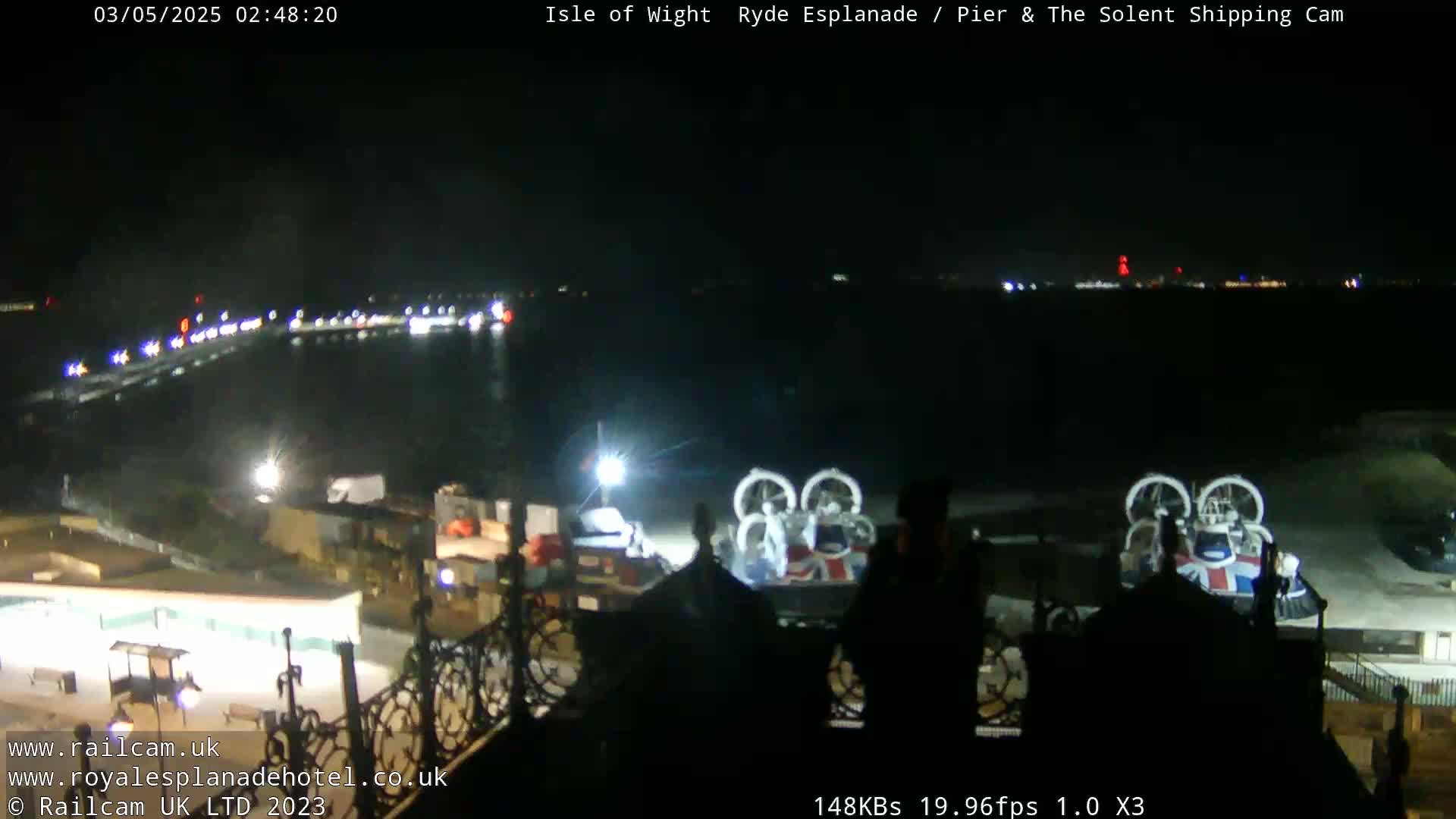 A nighttime view of a body of water with lights on the far shore and a hovercraft near a pier.