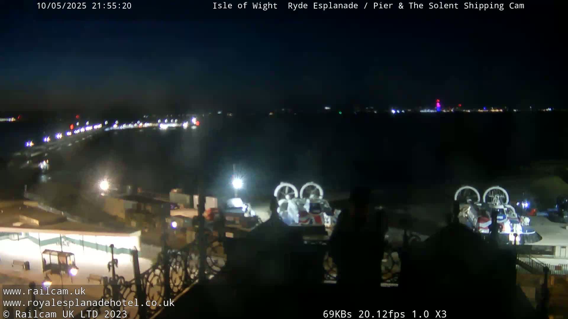 A nighttime view of a body of water with lights on the opposite shore, and two hovercrafts parked near a building.