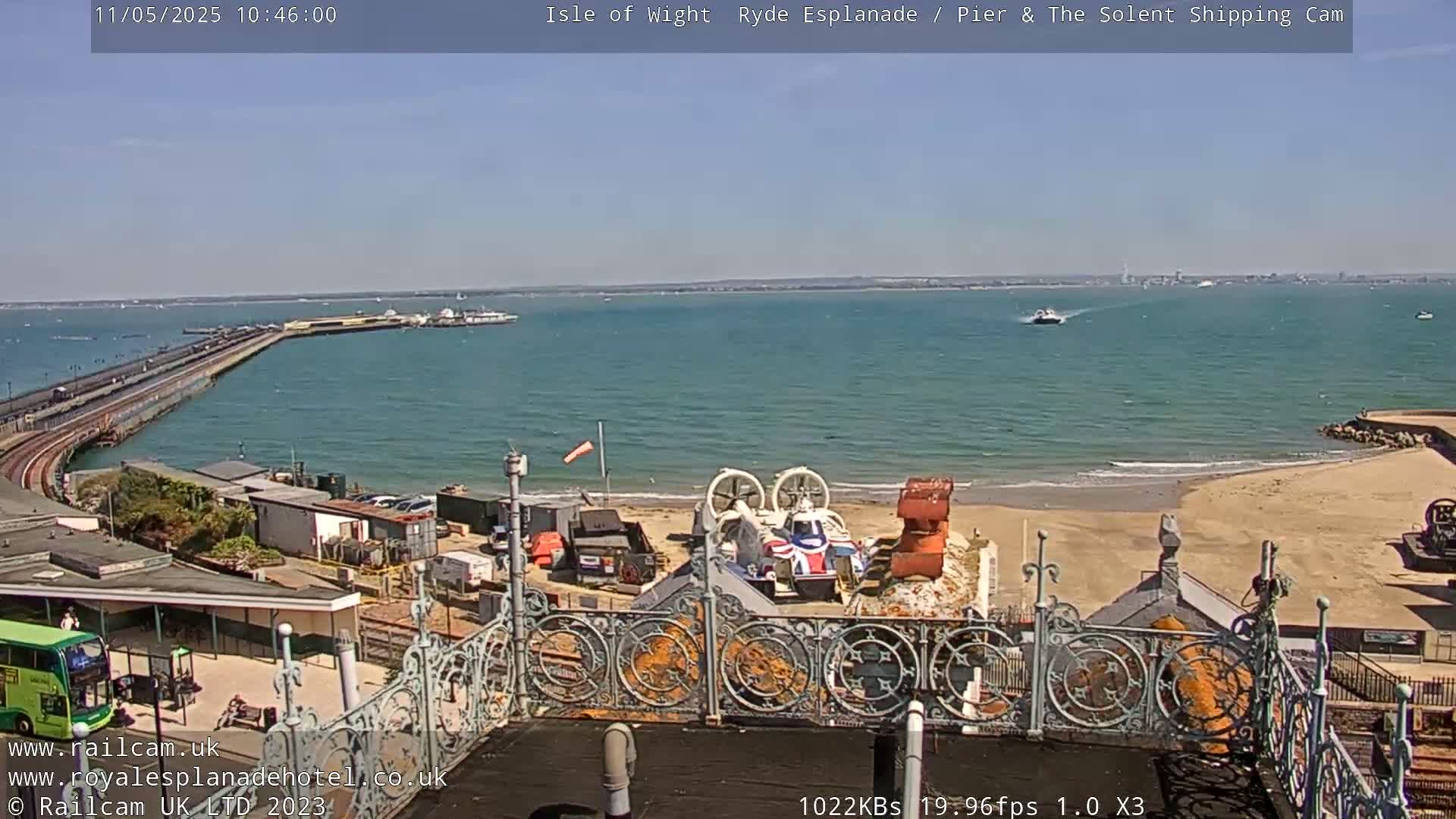 A hovercraft sits on a sandy beach near a pier extending into a calm, sunny ocean.